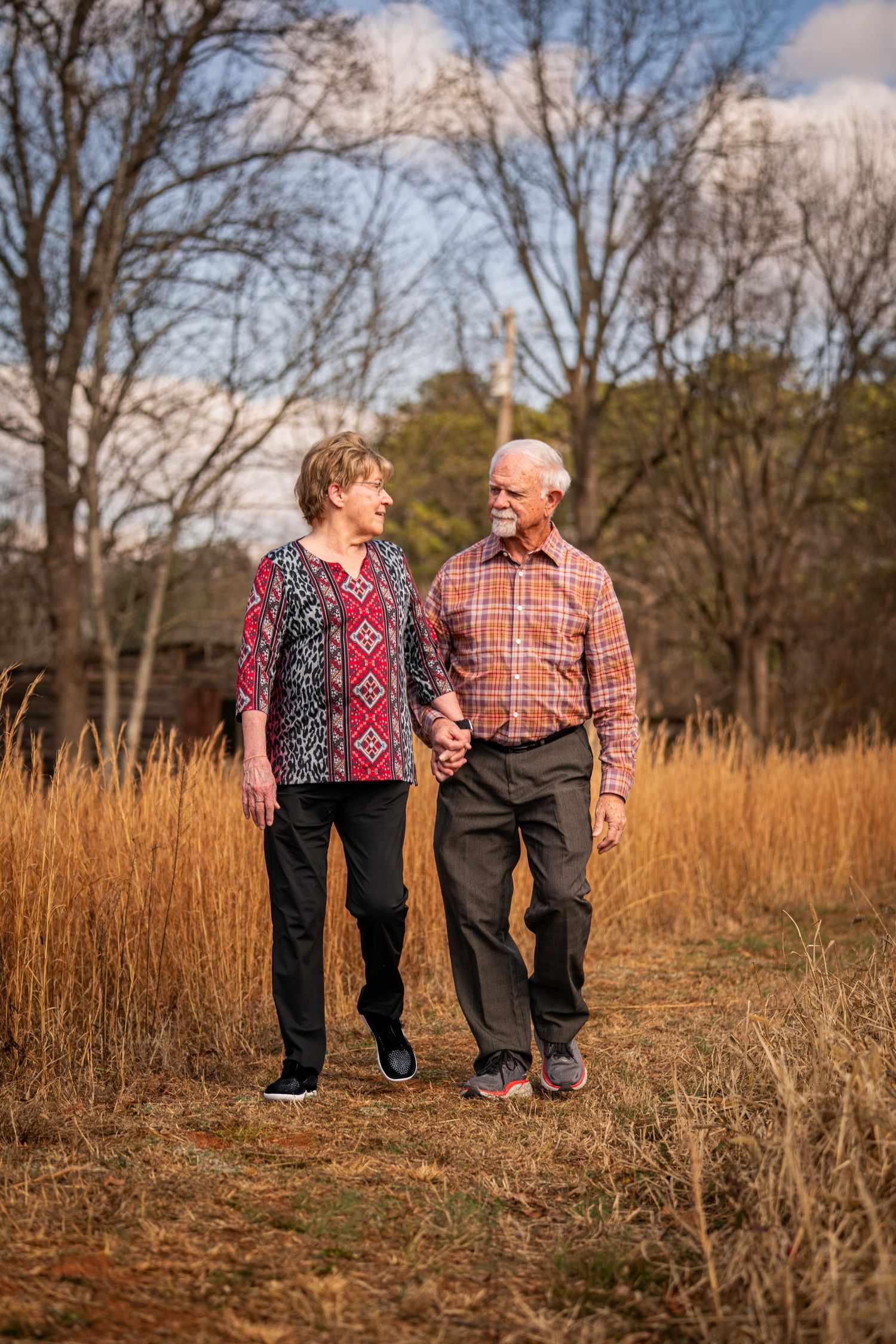 A couple walks together through a golden field of tall grass on an autumn afternoon.
