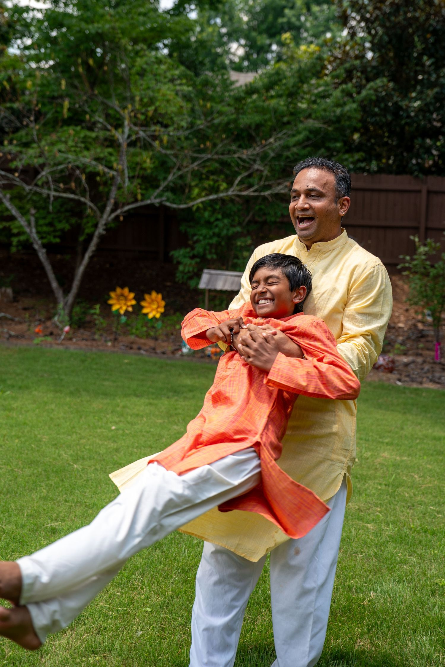 Indian father and son in traditional kurta outfits laughing and playing in a green backyard garden.