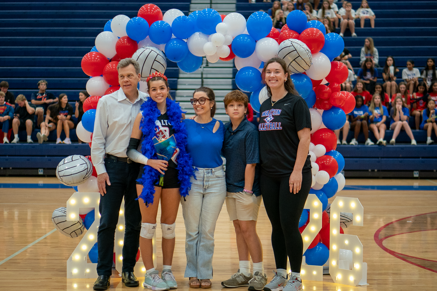 Athletes gather for team photo in gymnasium with festive red and blue balloon arch.