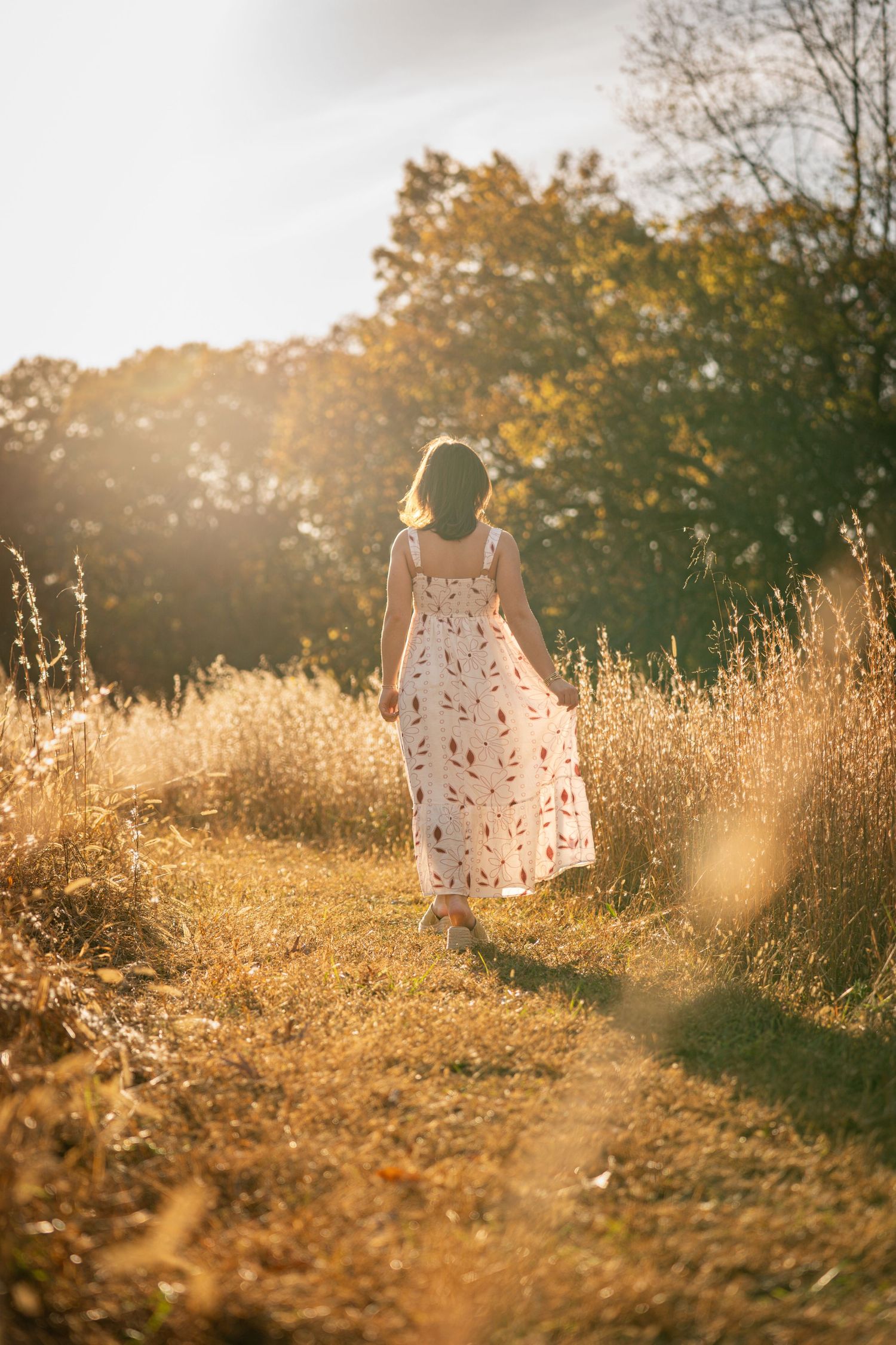 Dreamy golden hour sunlight illuminates a grassy meadow with a figure in a white dress standing in soft focus.