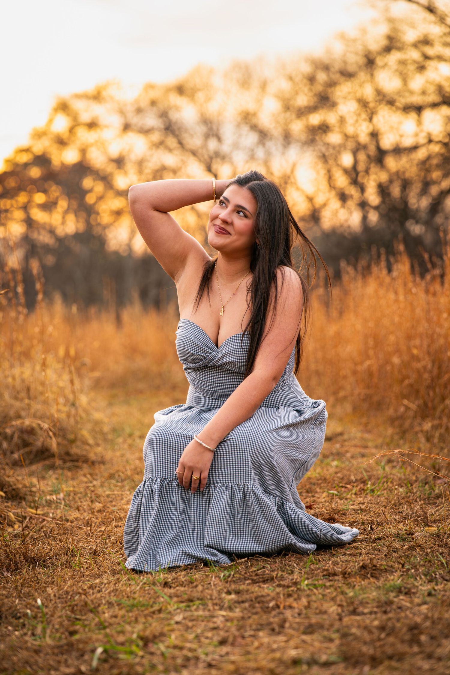 A person in a gray dress poses gracefully on autumn ground during golden hour sunset lighting.