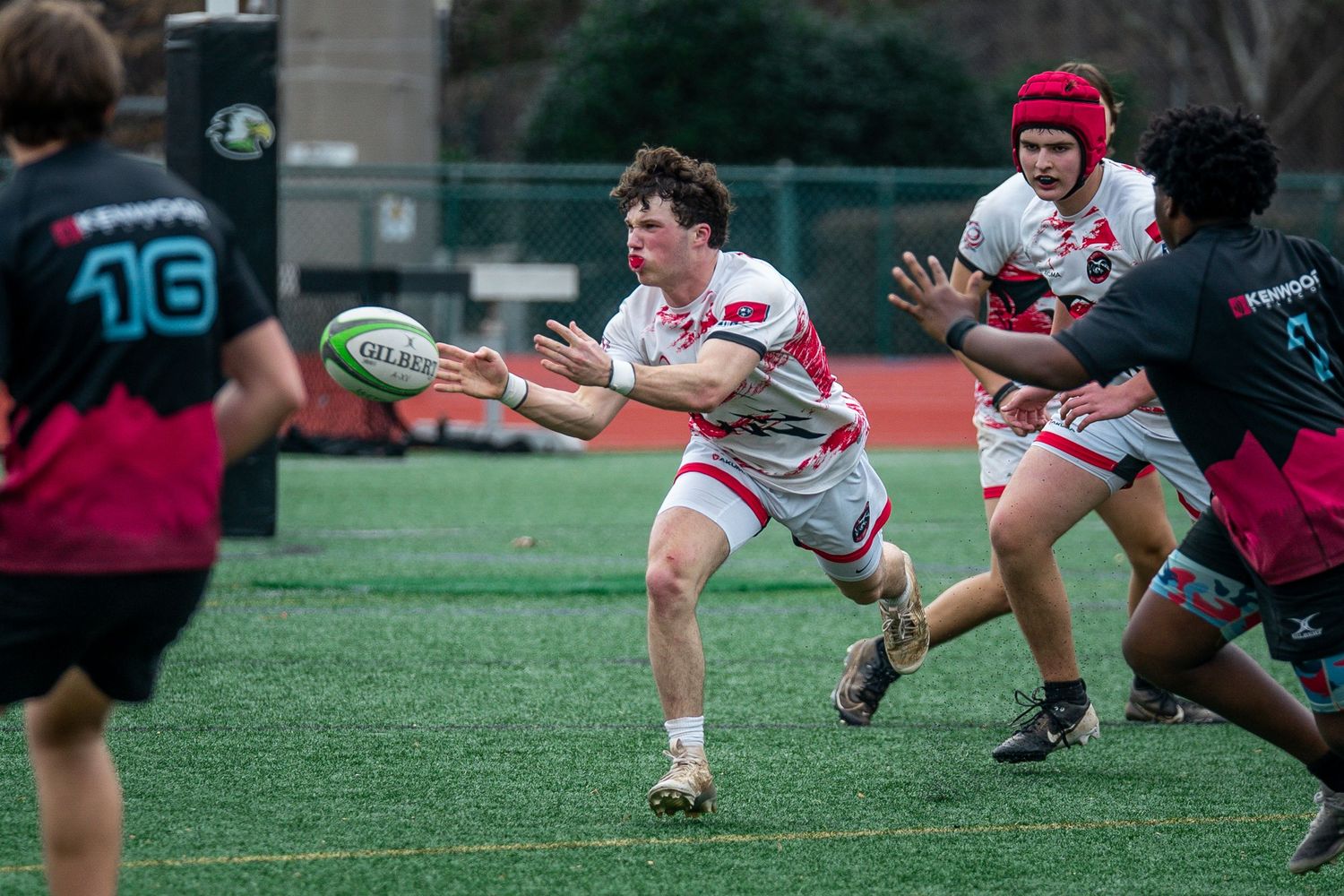 Rugby players dive and stretch for the ball during an intense match on a grass field.