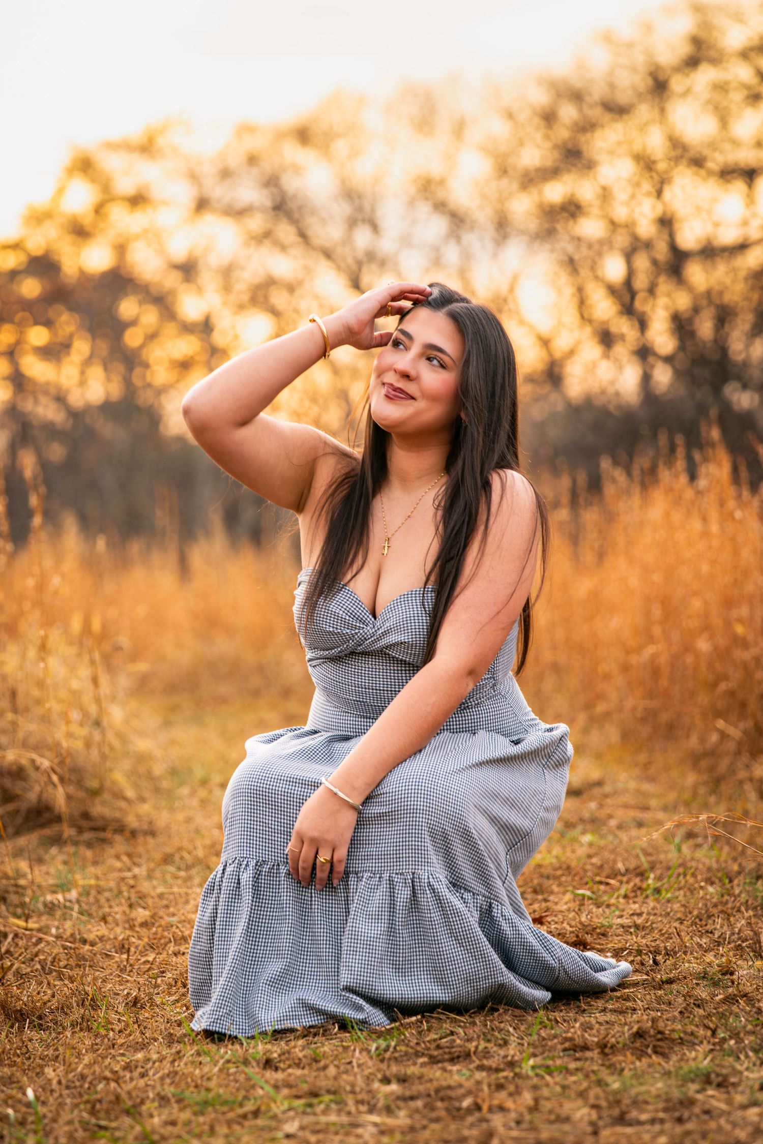 Pregnant woman in gray dress poses gracefully in golden autumn field during sunset maternity photoshoot.