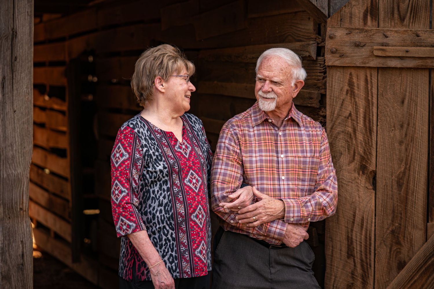 A couple shares a candid moment together while standing in front of rustic wooden barn walls.