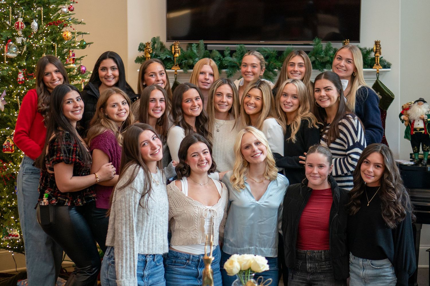 Group of people standing together and smiling in front of a decorated Christmas tree at a holiday gathering.