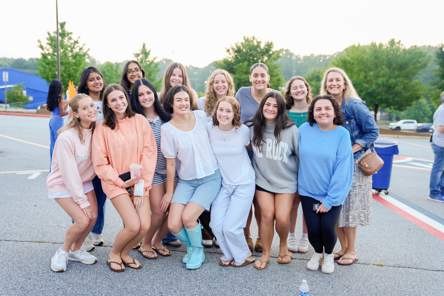 Group of teenage girls smiling and posing together in a parking lot during a casual outdoor gathering.