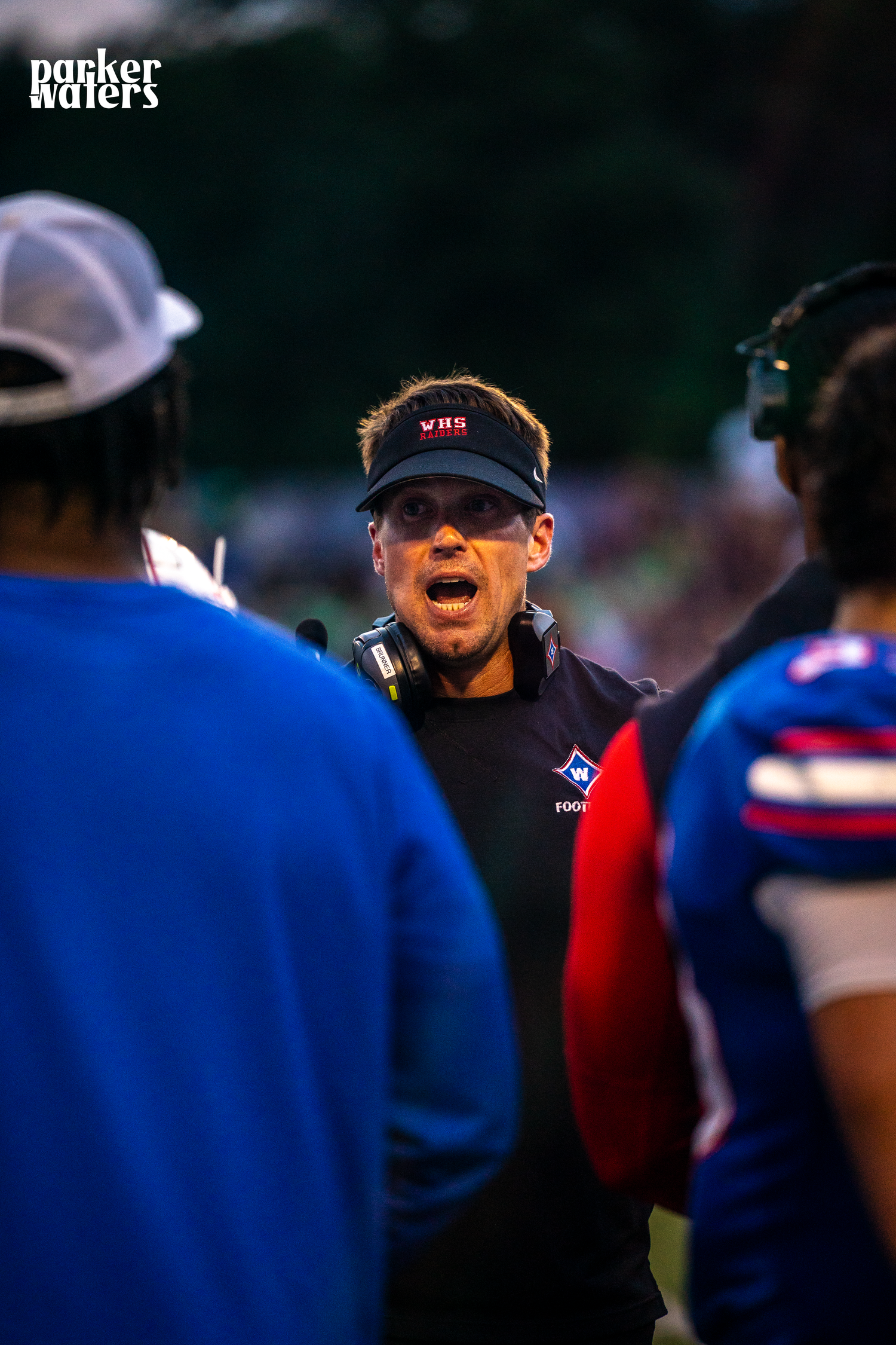 Coaches and players gather on the sidelines during a nighttime football game.