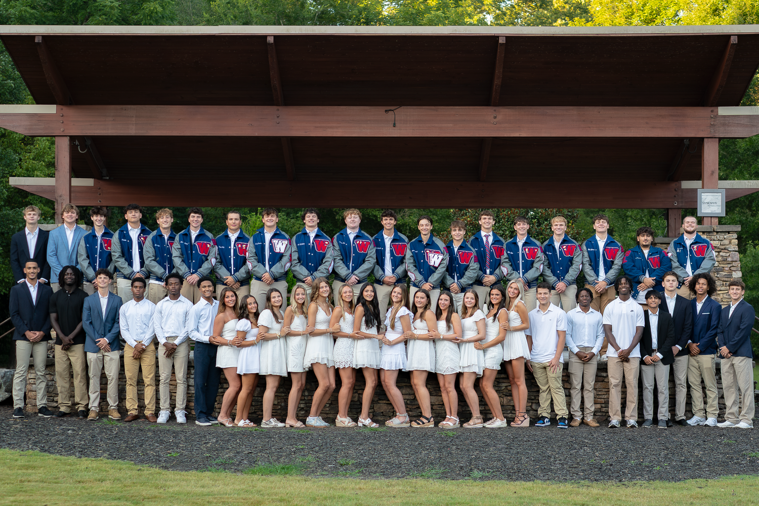 Row of students lined up against stone wall wearing coordinated outfits for group photo.