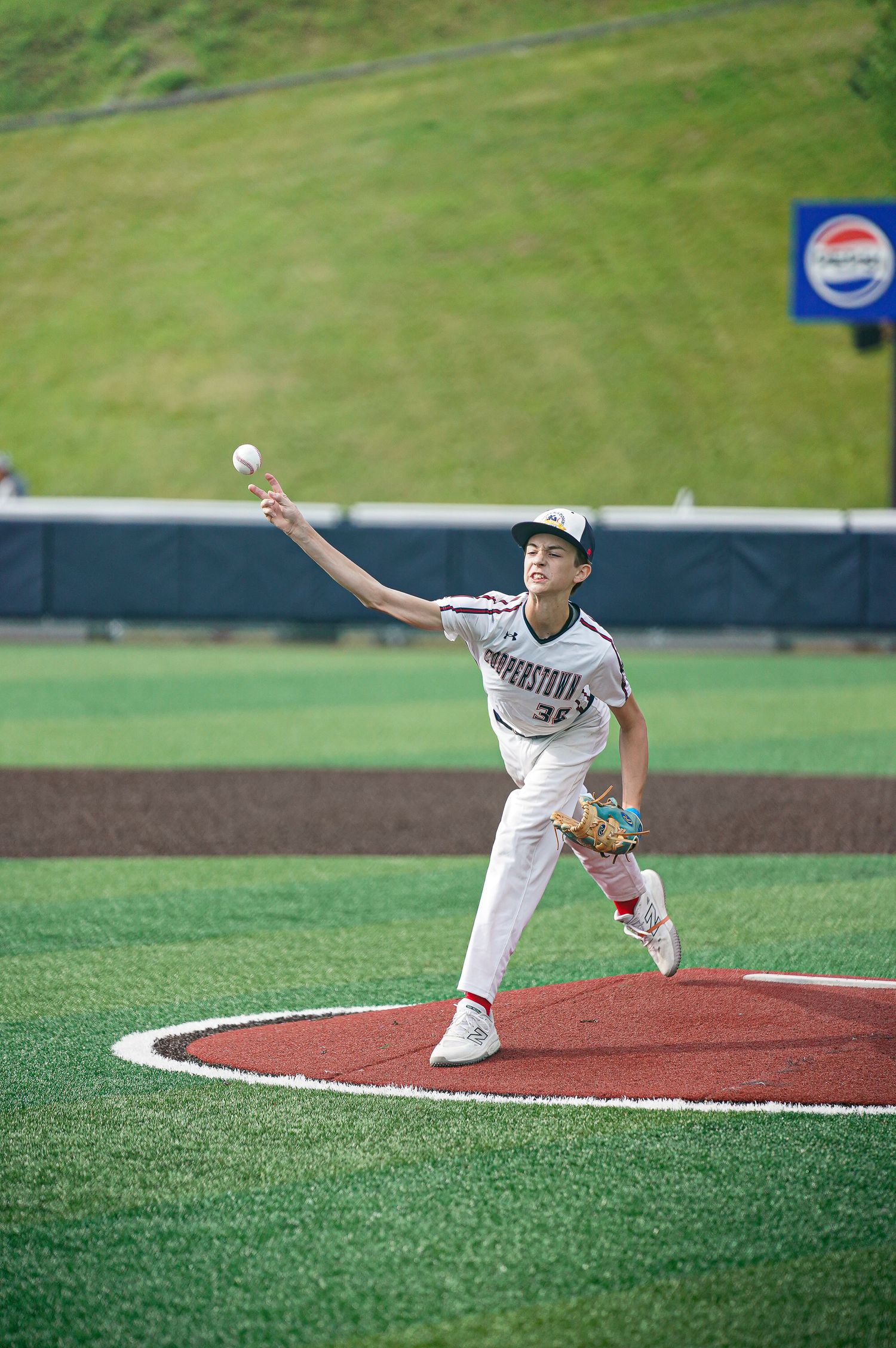 Baseball player in white uniform throwing pitch on red clay mound during game.