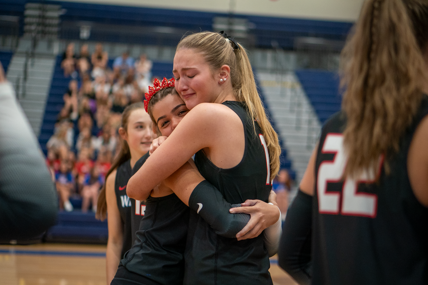 Athletes celebrate during volleyball game in gymnasium with decorative balloons.