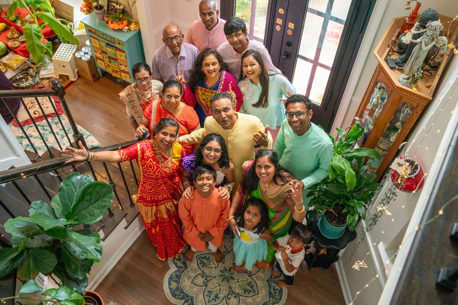 Large multigenerational Indian family gathered indoors, smiling and posing together on a staircase landing for a festive celebration.