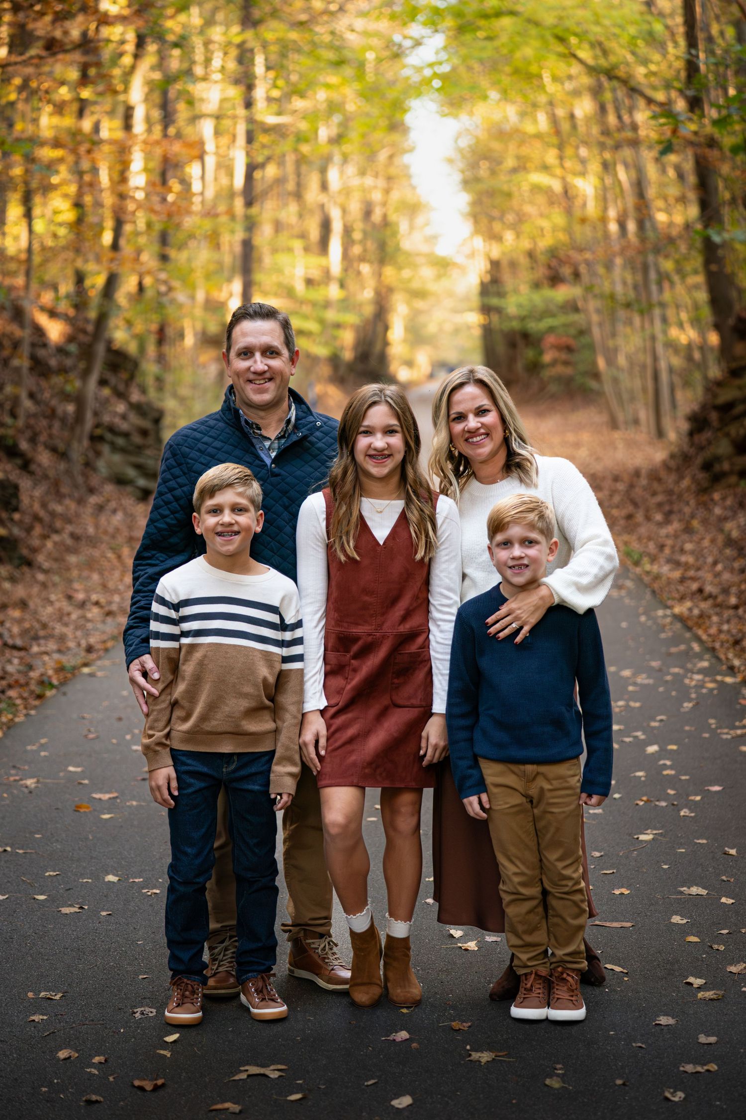 Family photo session on an autumn path with siblings in coordinated casual outfits.