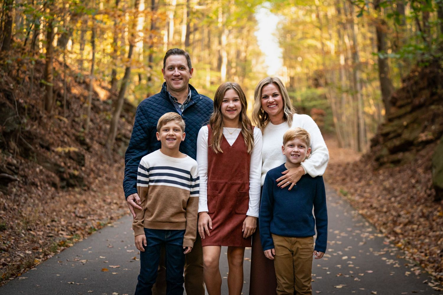 Family portrait session in a beautiful autumn forest setting with warm golden light filtering through the trees.