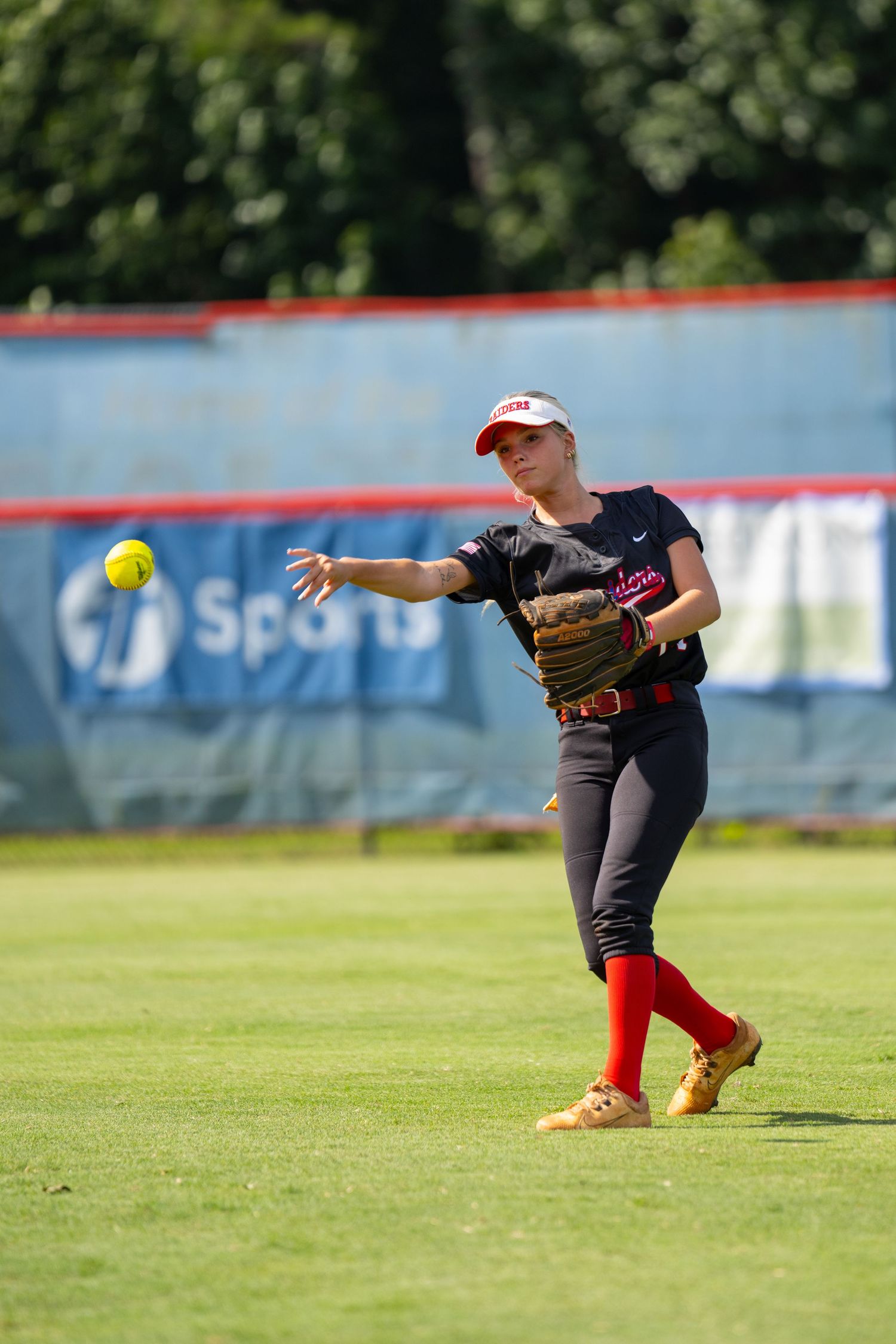 Female softball player in black uniform throwing ball on green field during competitive game outdoors.