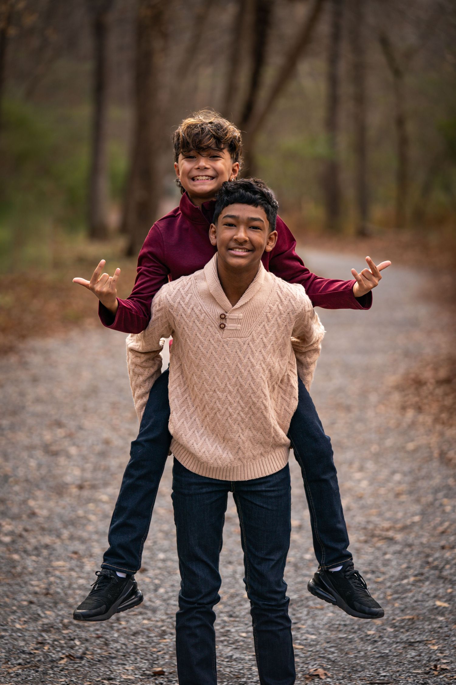 Two people playfully pose together on a path in autumn, one wearing a beige sweater and the other in dark clothing.