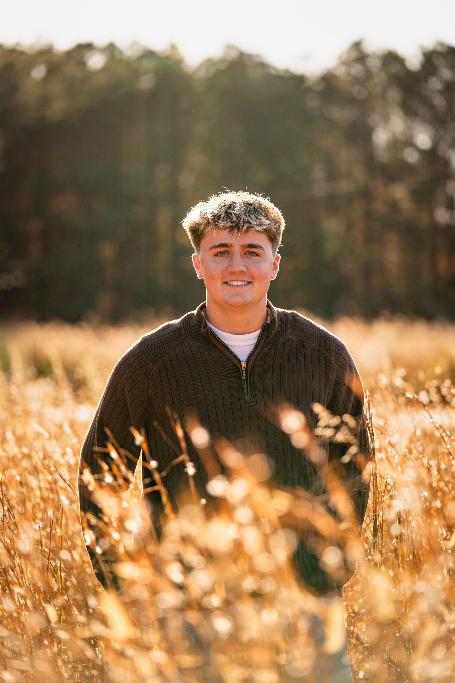A person in a dark sweater stands in a golden field during sunset with soft lighting and bokeh effect.
