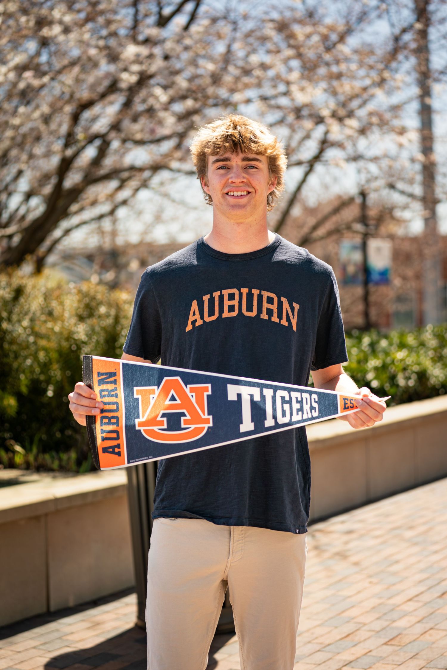 Auburn University student displays school spirit with navy blue shirt and Tigers pennant on sunny spring day.