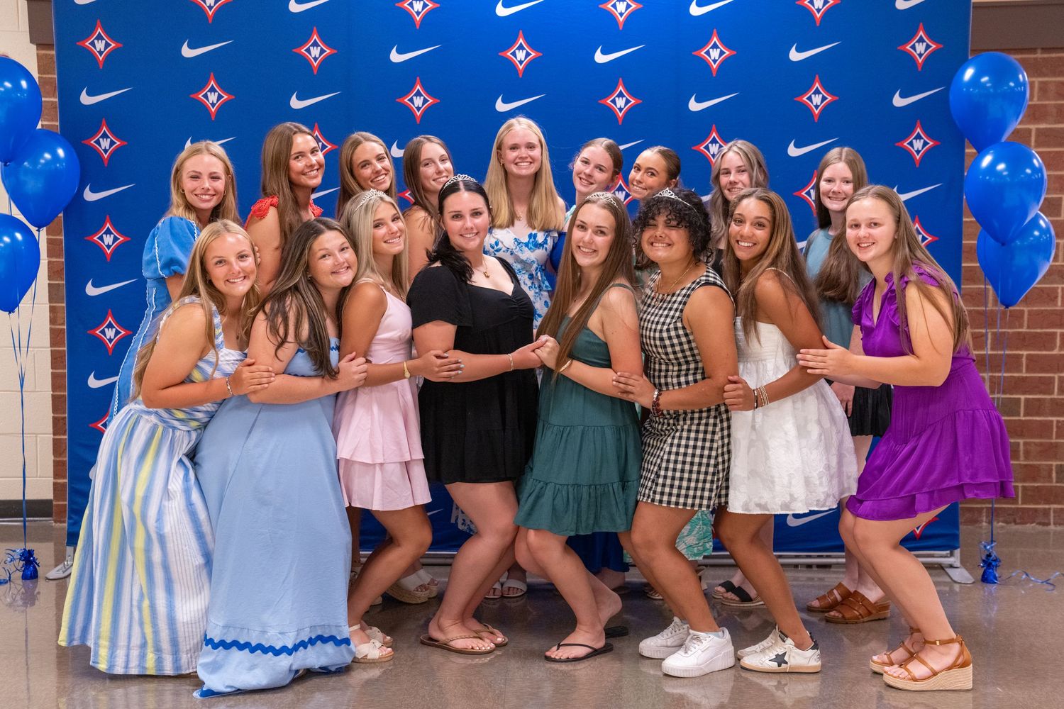 Group of young women in colorful dresses posing together at a Nike-sponsored event with blue balloons.