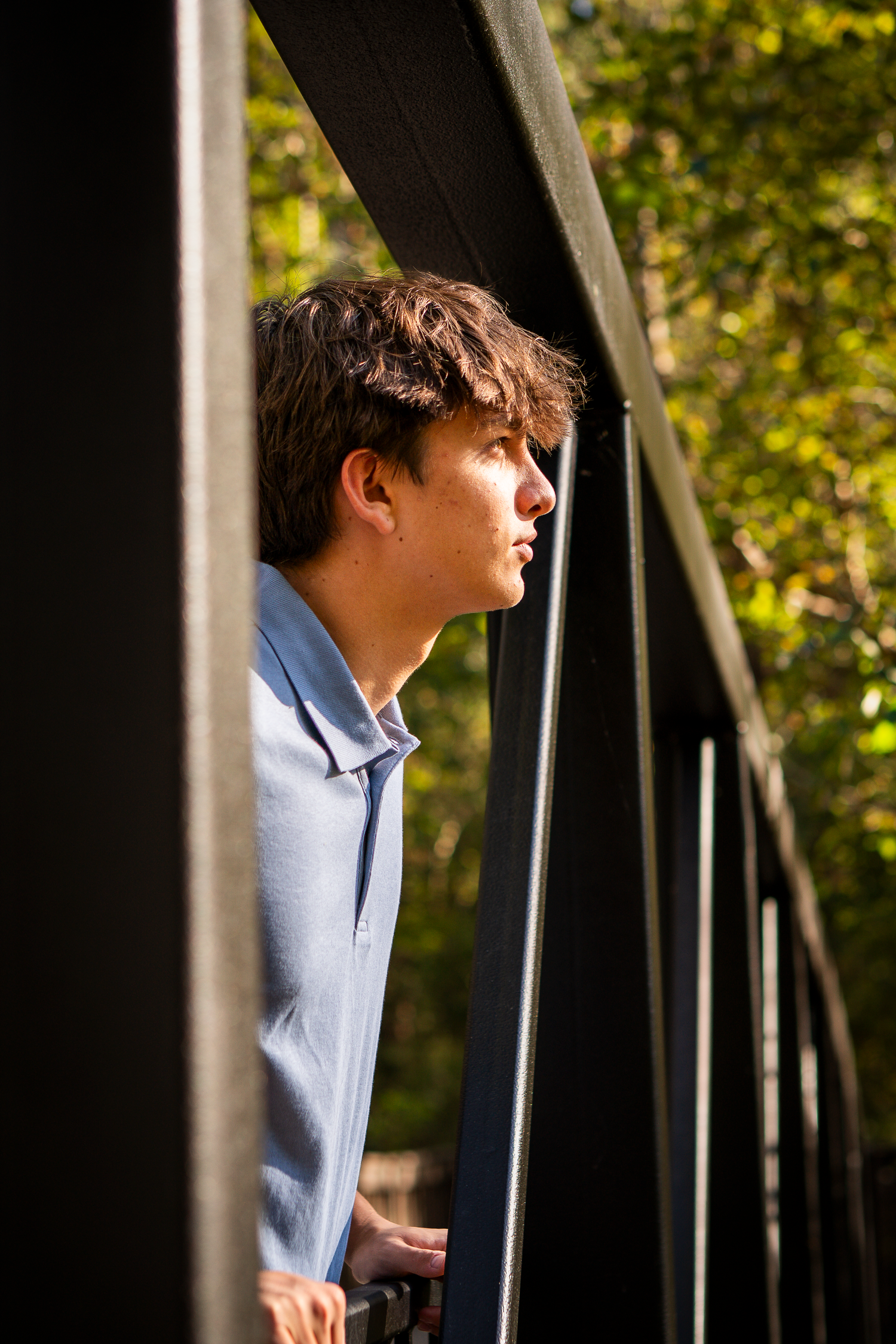 Artistic portrait on a bridge with dramatic side lighting and metal railings.
