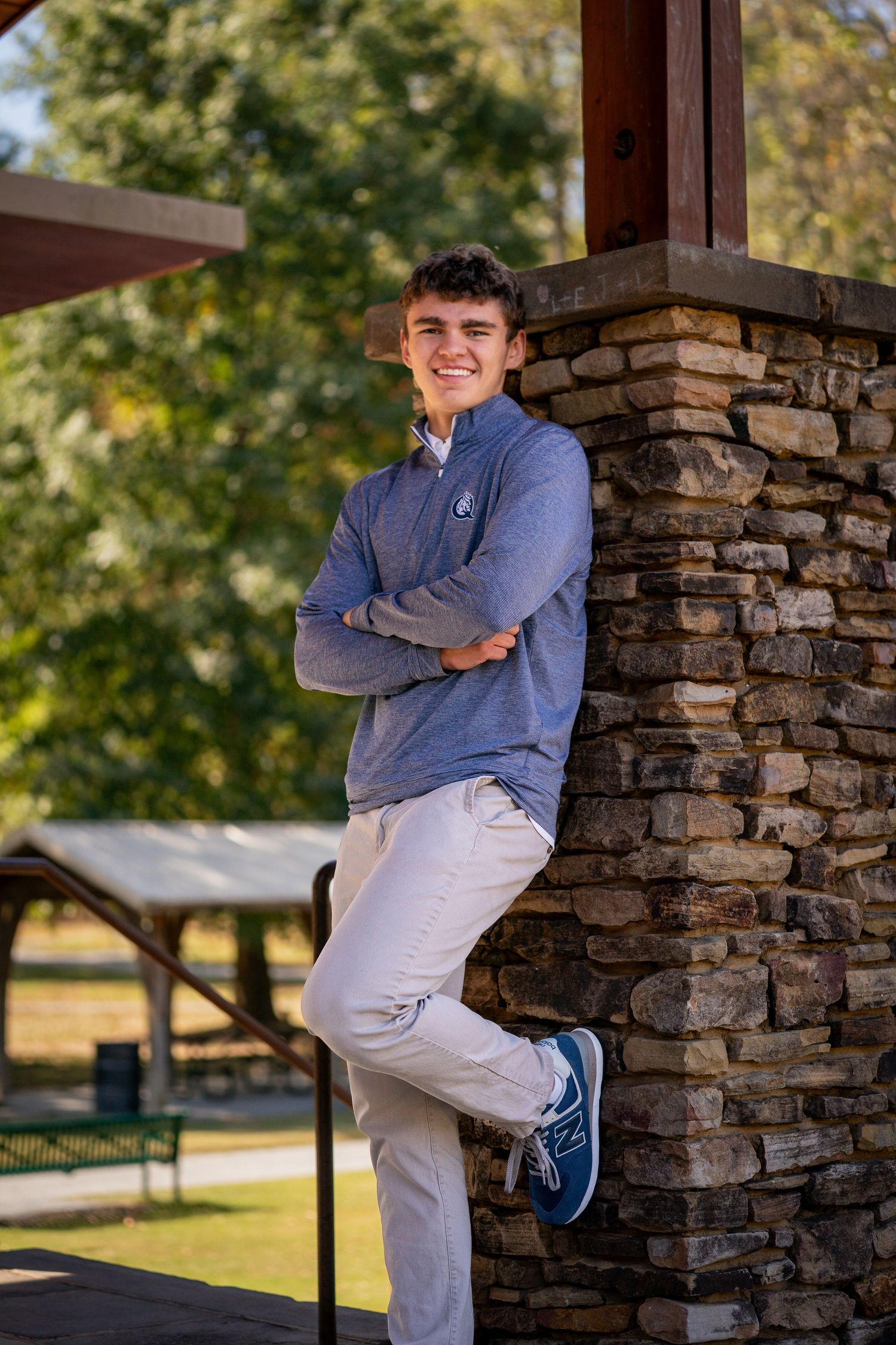 Student in blue sweater and khakis leans casually against stone pillar outdoors.