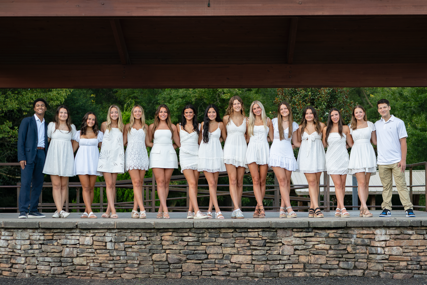 Group portrait of students arranged along a stone wall in matching attire.