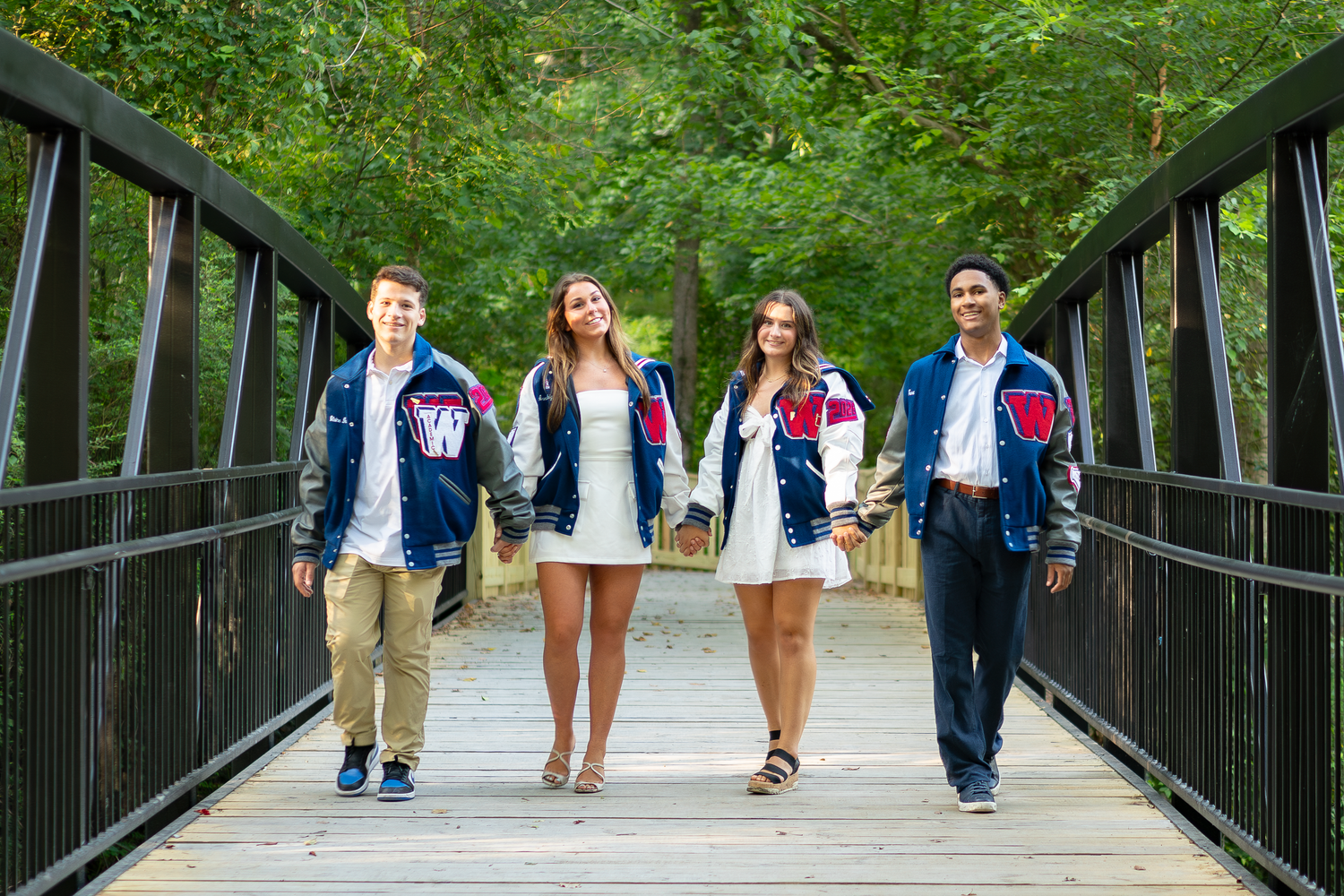 Students walking together across wooden bridge pathway in park setting.