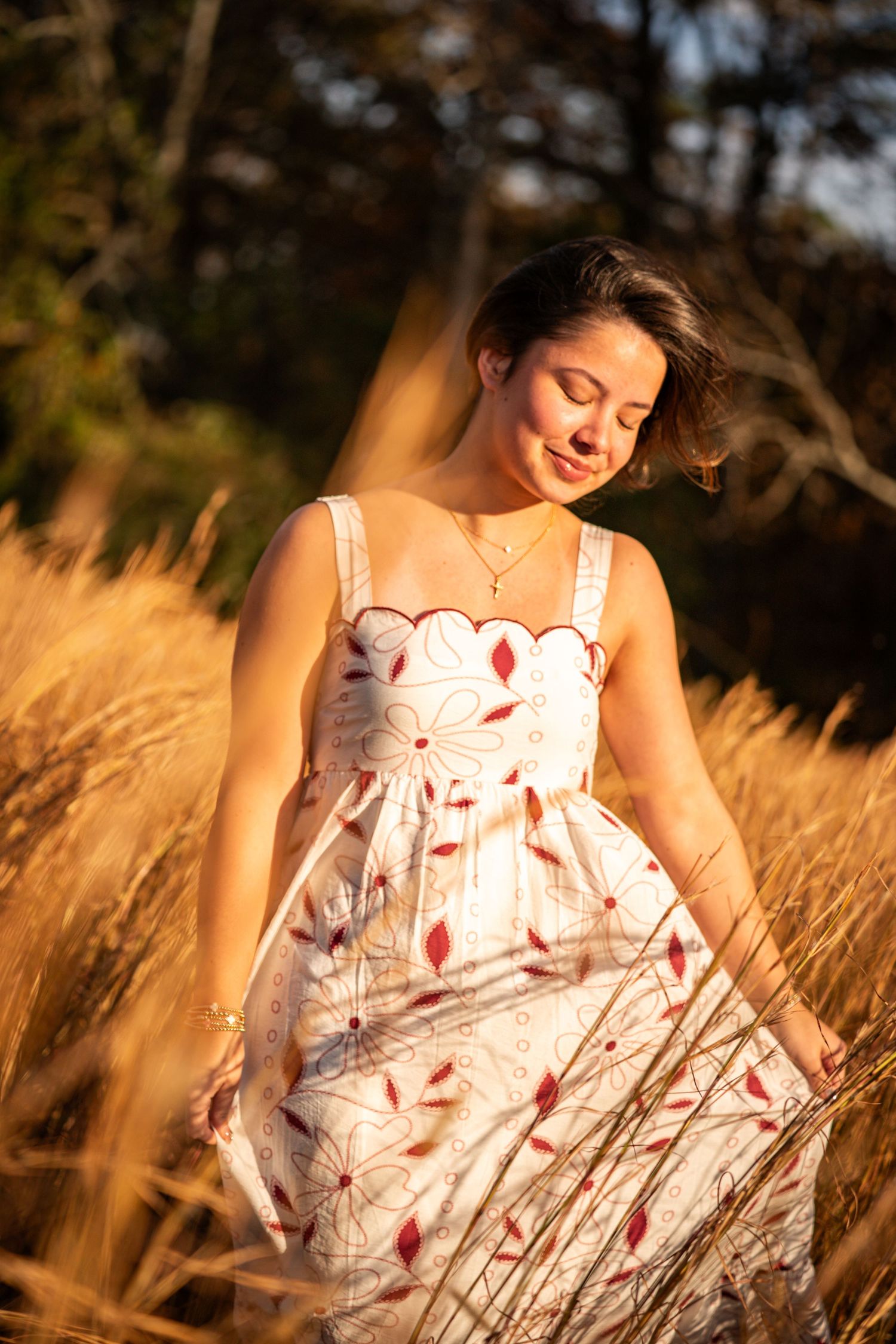 Young woman in white floral dress standing in golden wheat field during sunset.