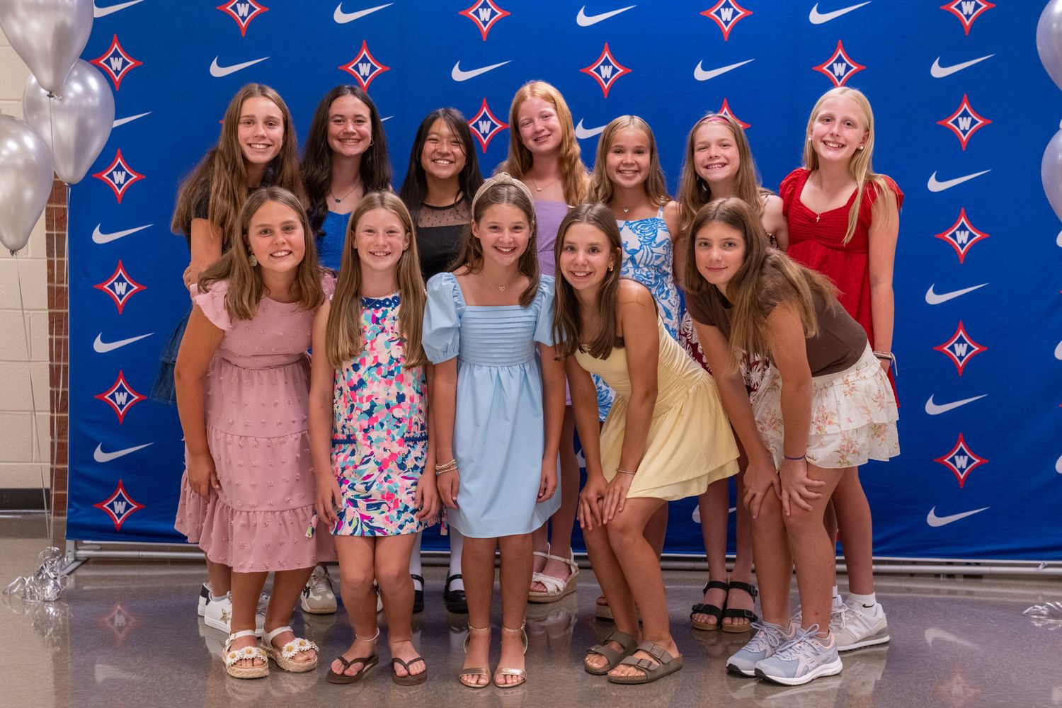 Group of young girls posing together in front of a Nike-branded blue backdrop at a sports recognition event.