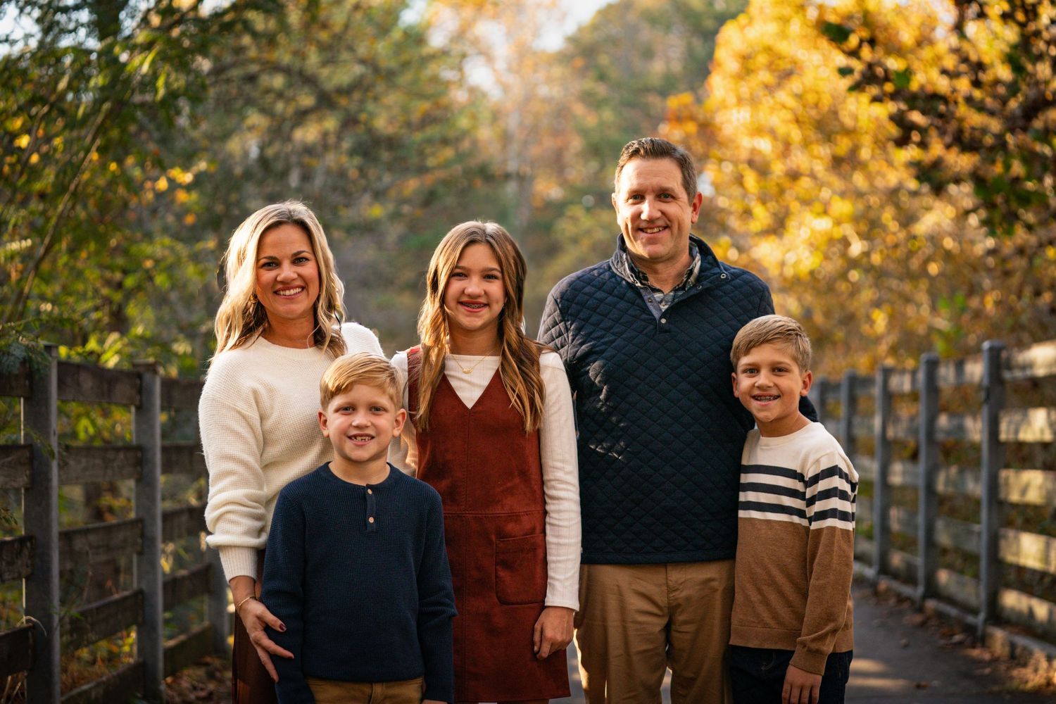 Family poses together on wooden bridge during golden autumn afternoon.