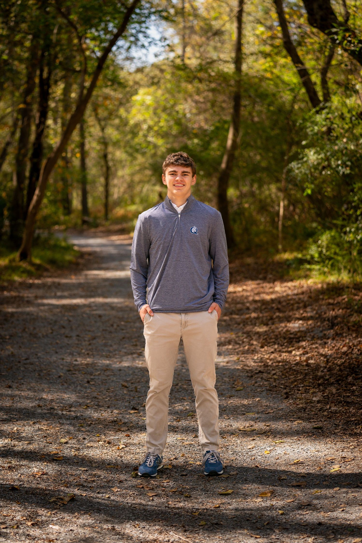 Portrait session on a tree-lined path with autumn leaves scattered on the ground.