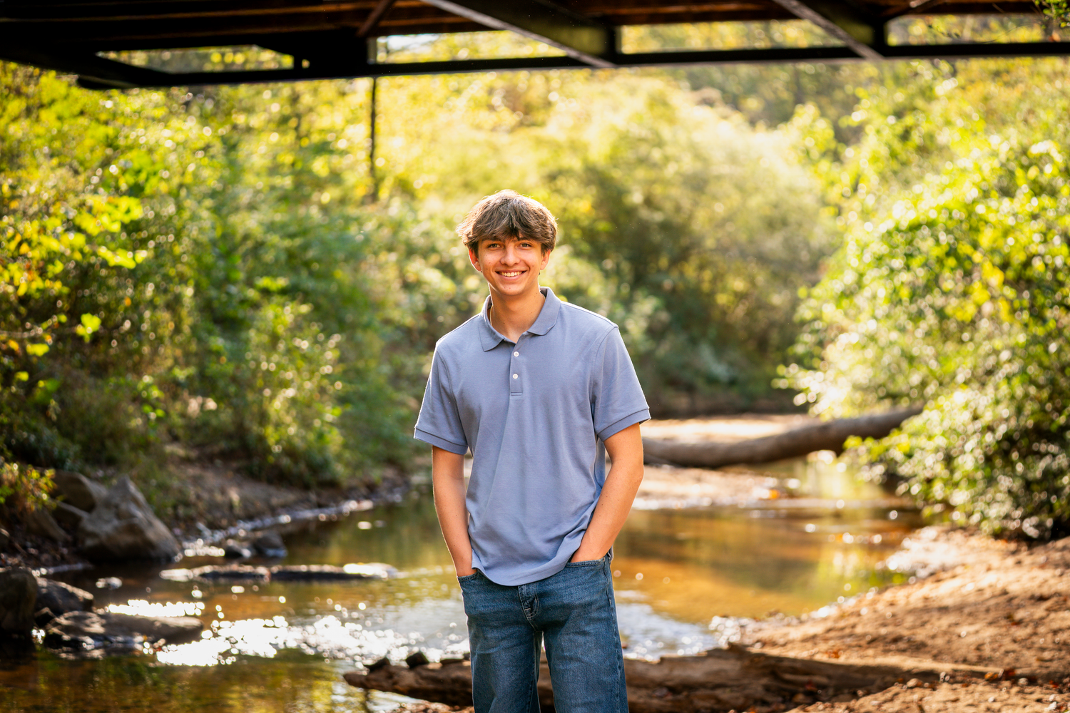 Portrait session in a natural outdoor setting with golden sunlight filtering through trees.