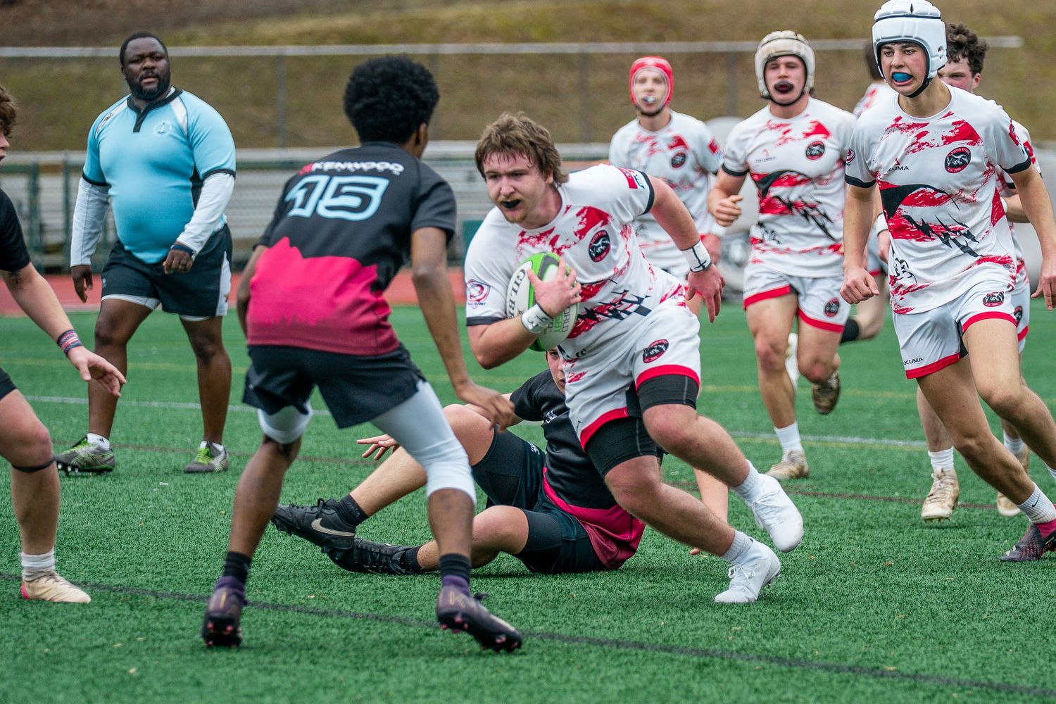 Rugby players in white and pink jerseys compete during an intense match on artificial turf field.