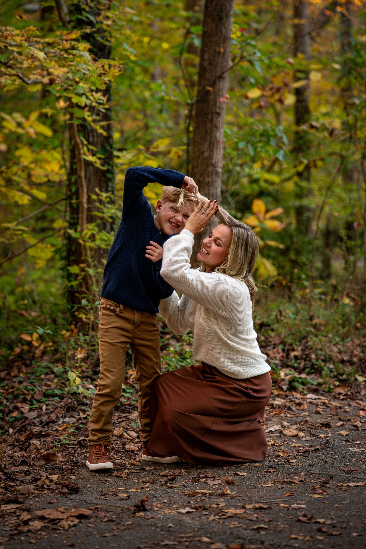 Playful family moment captured on a leaf-covered forest path during autumn.