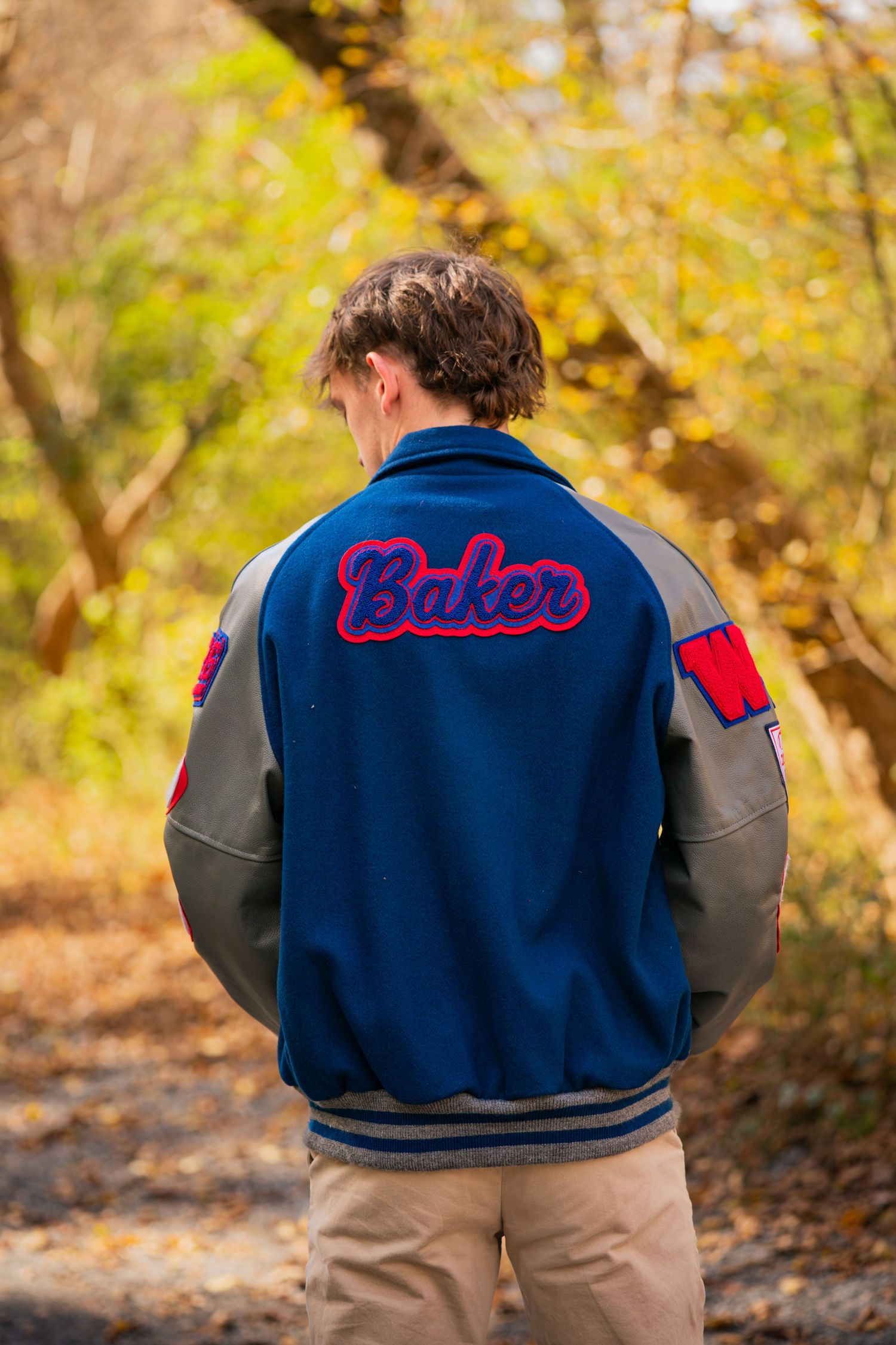 Back view of blue and gray varsity jacket with Baker lettering in autumn setting.