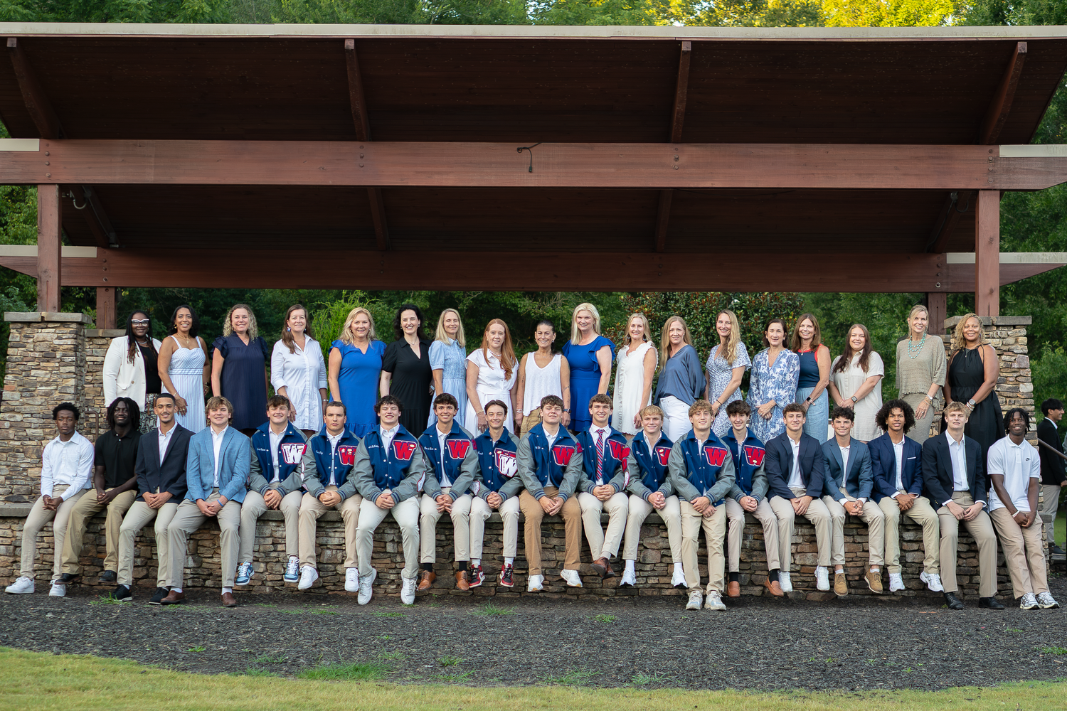 Panoramic group photo of people arranged in a line on stone wall wearing coordinated attire.
