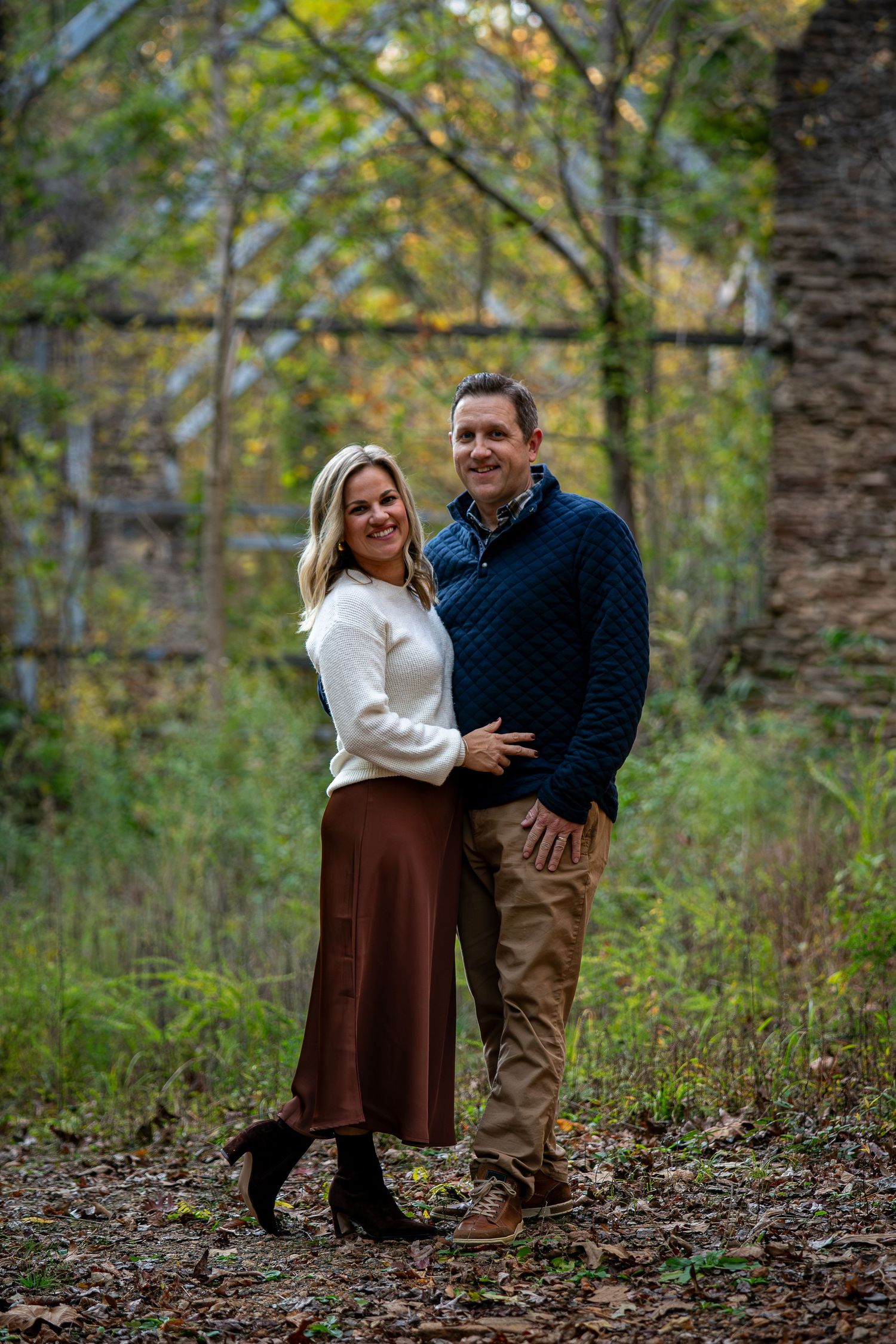 Candid moment captured between family members on a leaf-covered forest path in autumn.