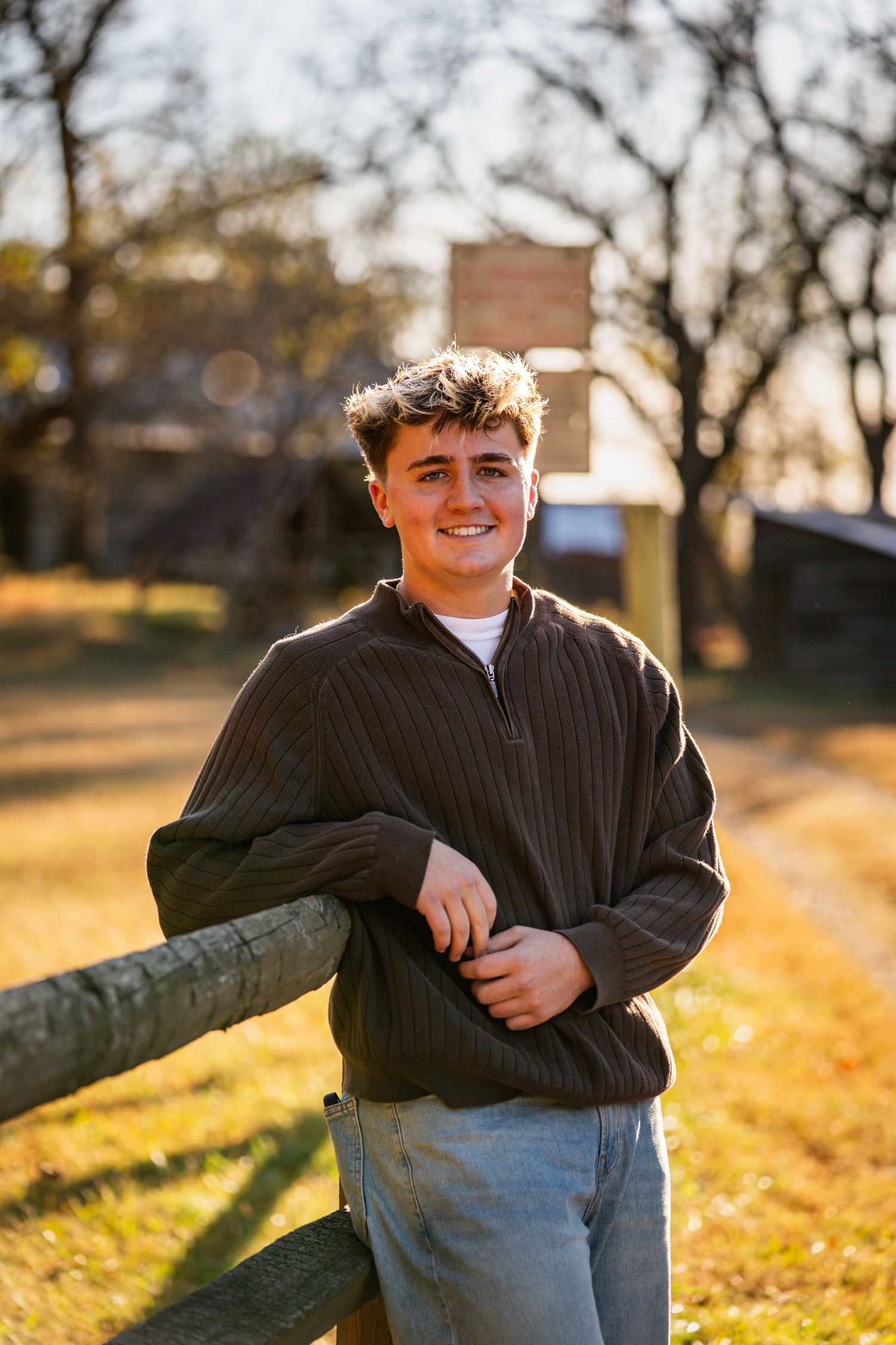 A person in a dark sweater sits on a fallen tree trunk during golden hour in autumn.