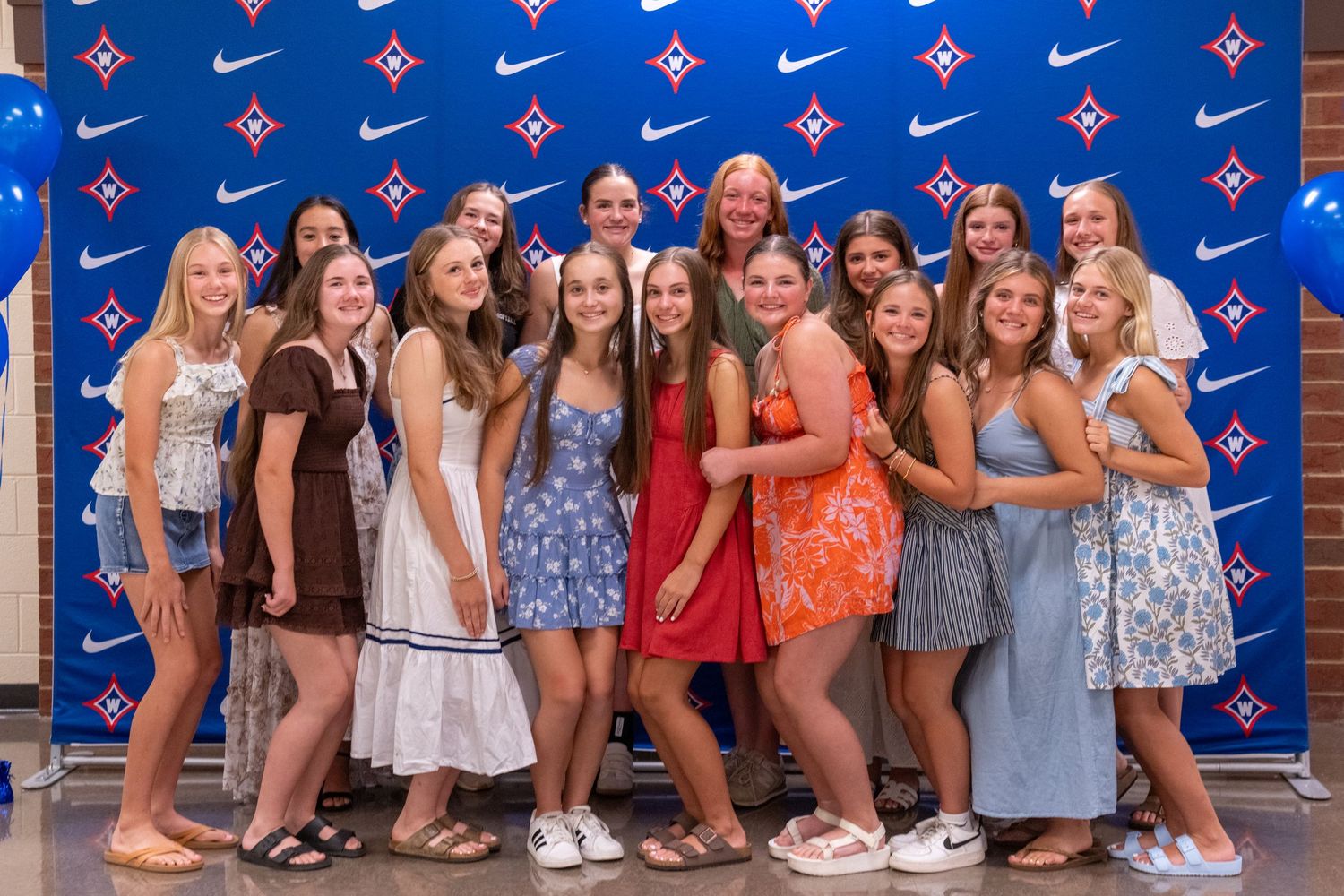 Group of teenage girls posing together in front of a Nike backdrop at a sports banquet event.