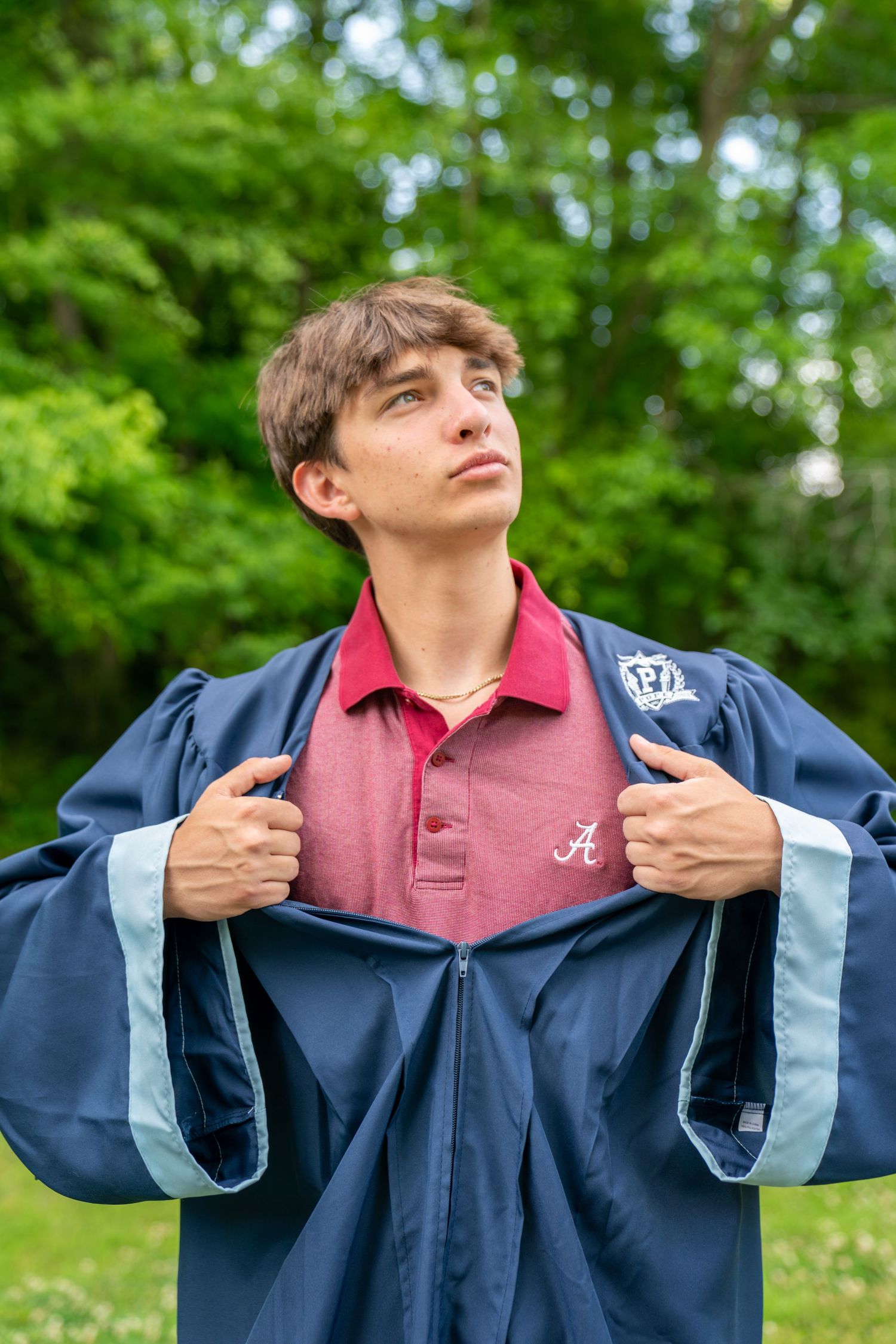 Young man dramatically opening navy graduation gown to reveal University of Alabama shirt outdoors.