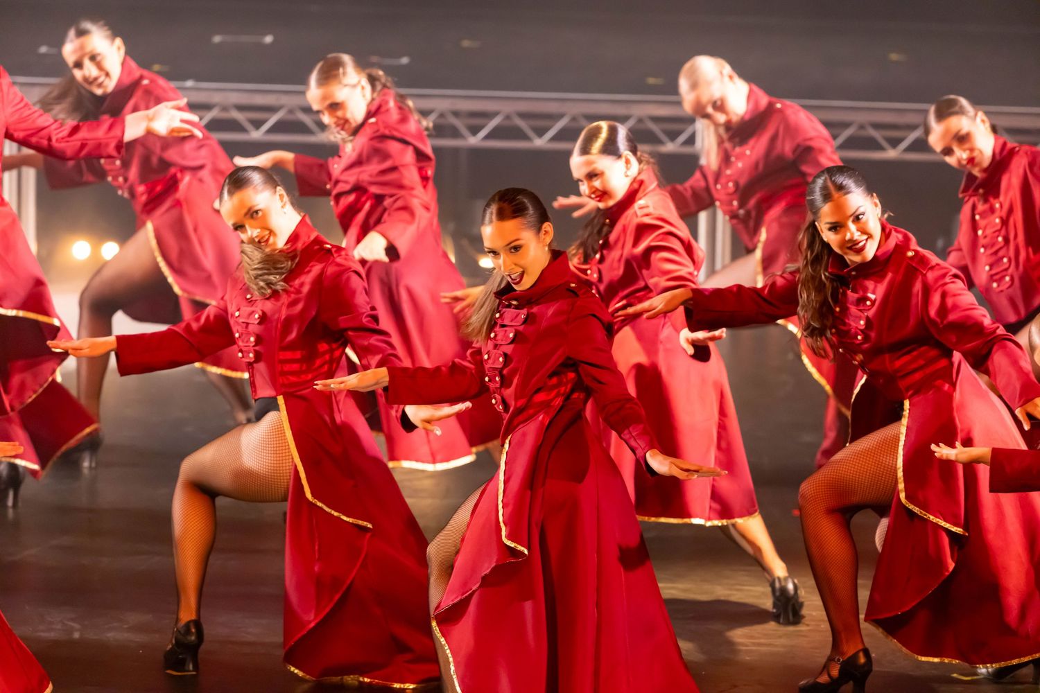 Performers in bright red costumes execute synchronized dance moves under stage lights.