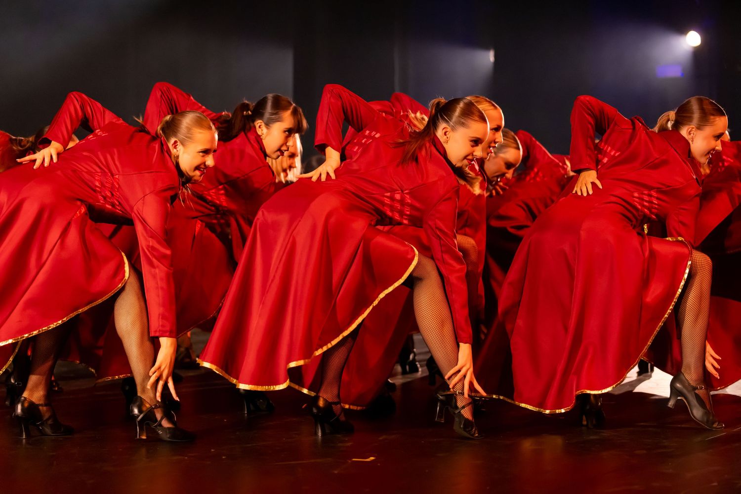 Dancers in flowing red dresses create a dramatic visual pattern during stage performance.
