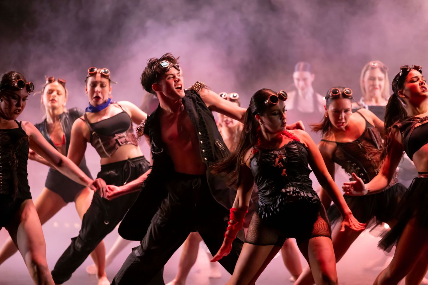 Dance ensemble performs dynamic movements in formation under dramatic stage lighting.