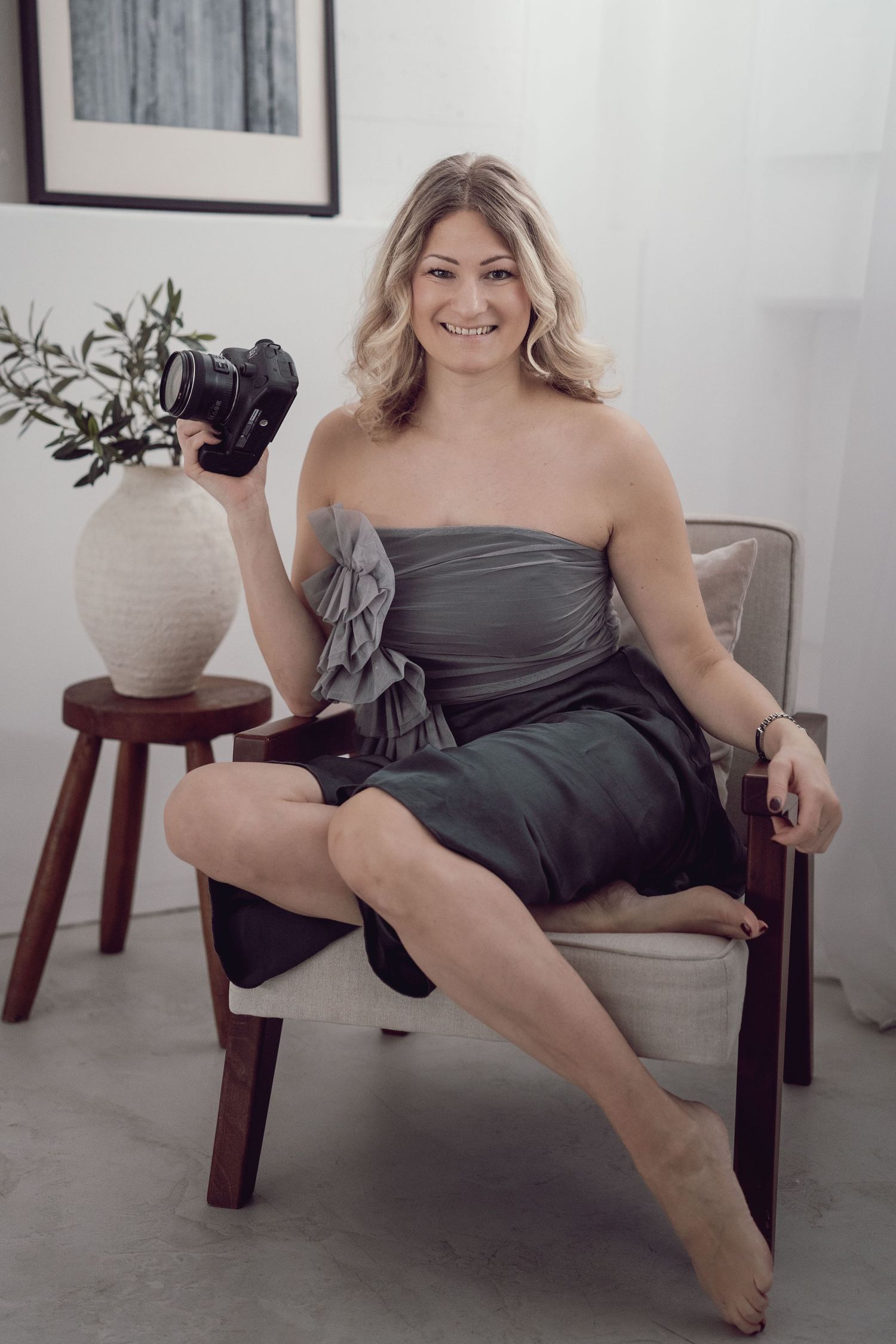 Jacky, Boudoir-Fotografin aus Dortmund, lächelt mit ihrer Kamera in einem stilvoll eingerichteten Studio.