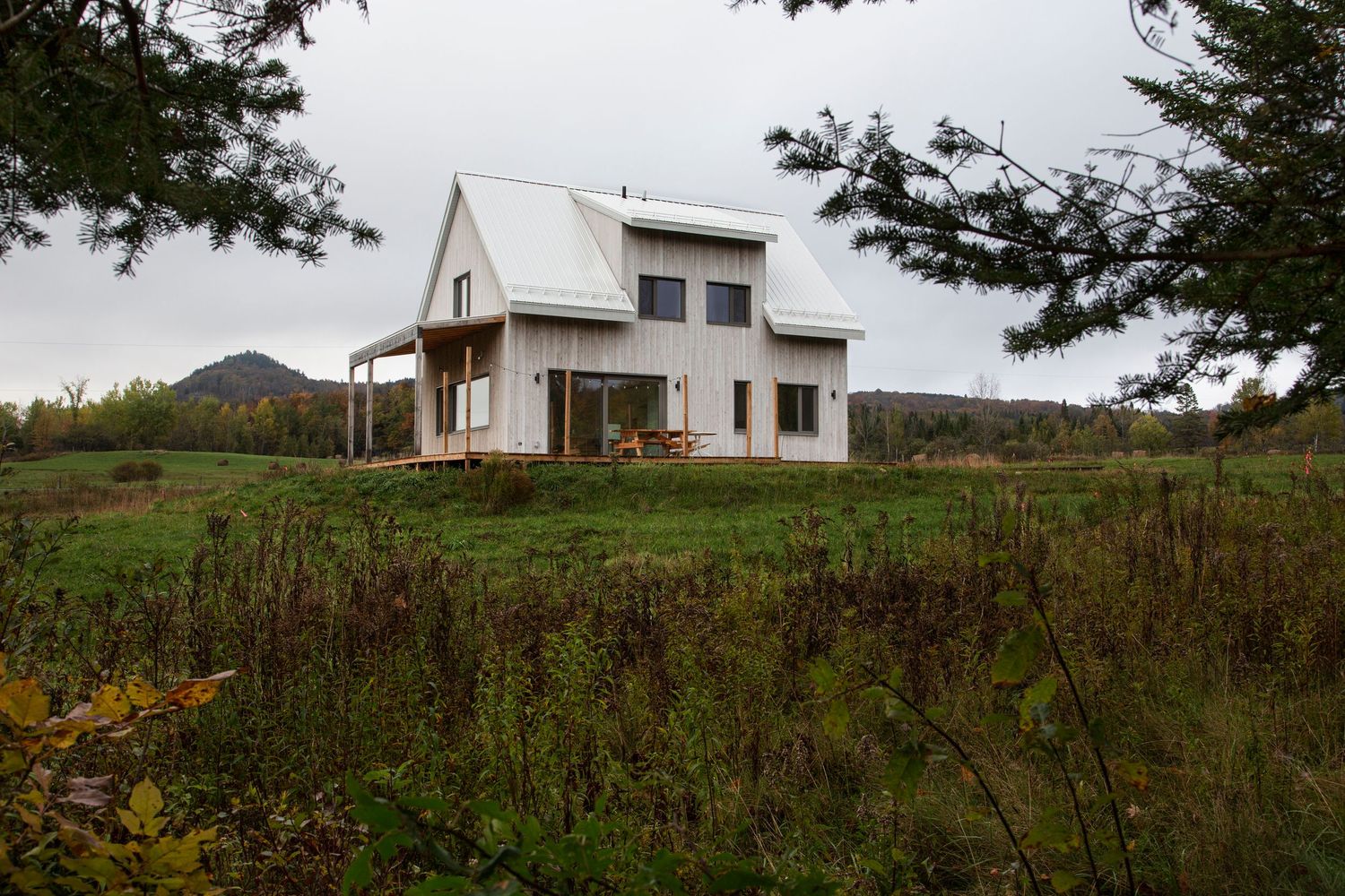 Modern rural house with wooden siding set against rolling green hills.