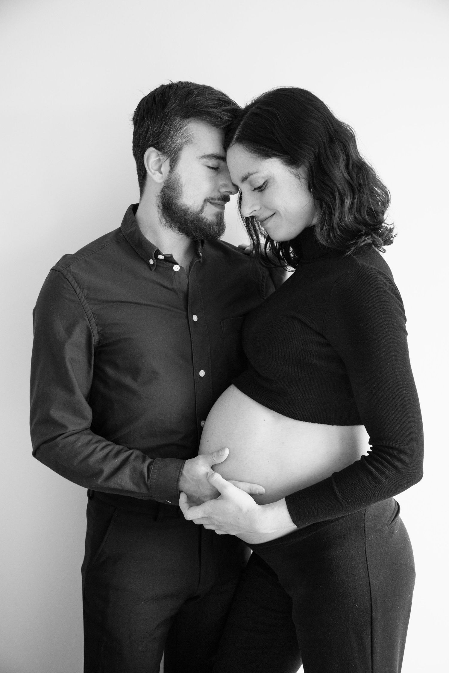 Intimate black and white maternity photoshoot series showing loving embrace between expectant parents.