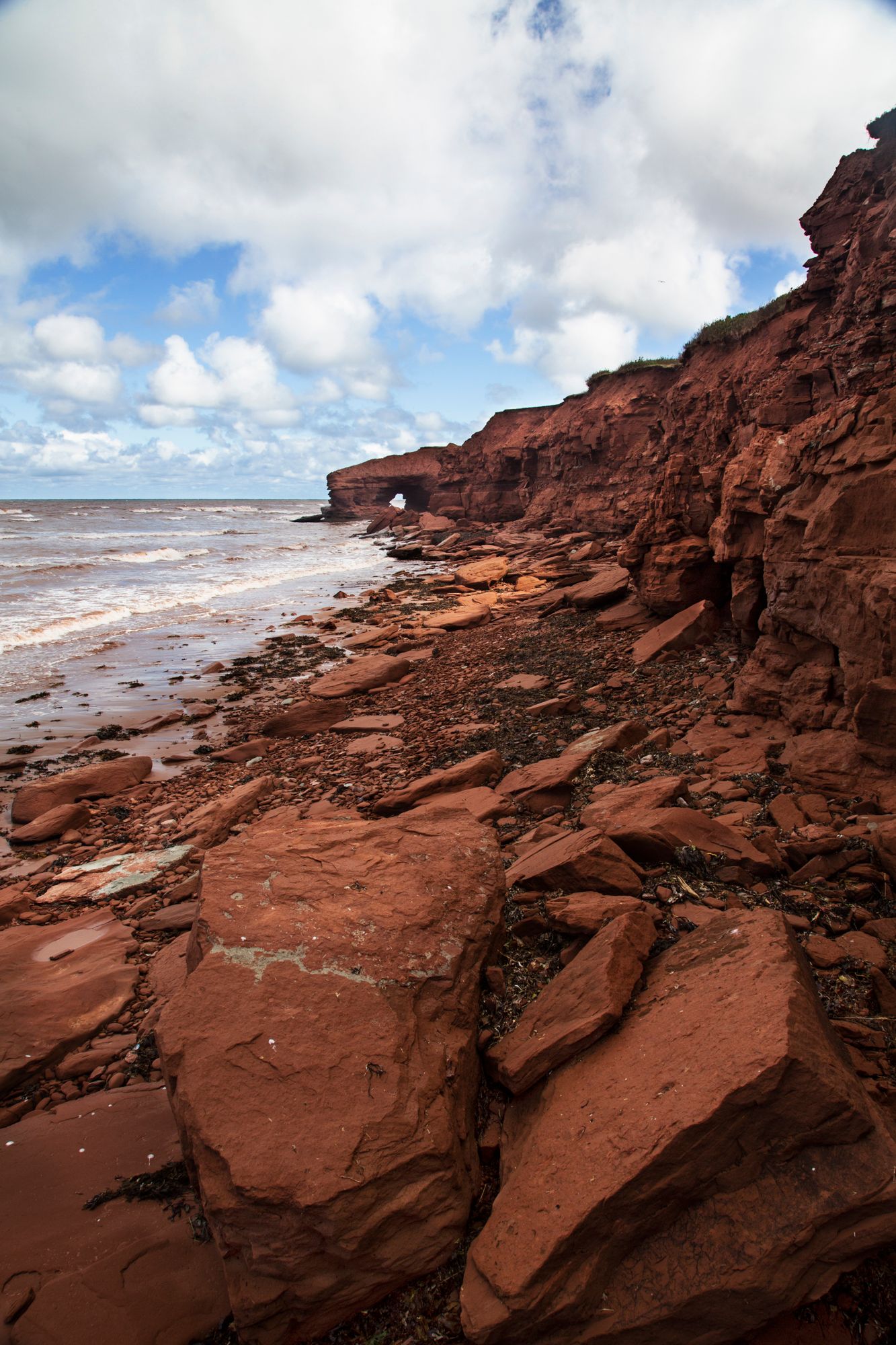 Red sandstone cliffs and rocky formations line a dramatic coastline under blue skies.