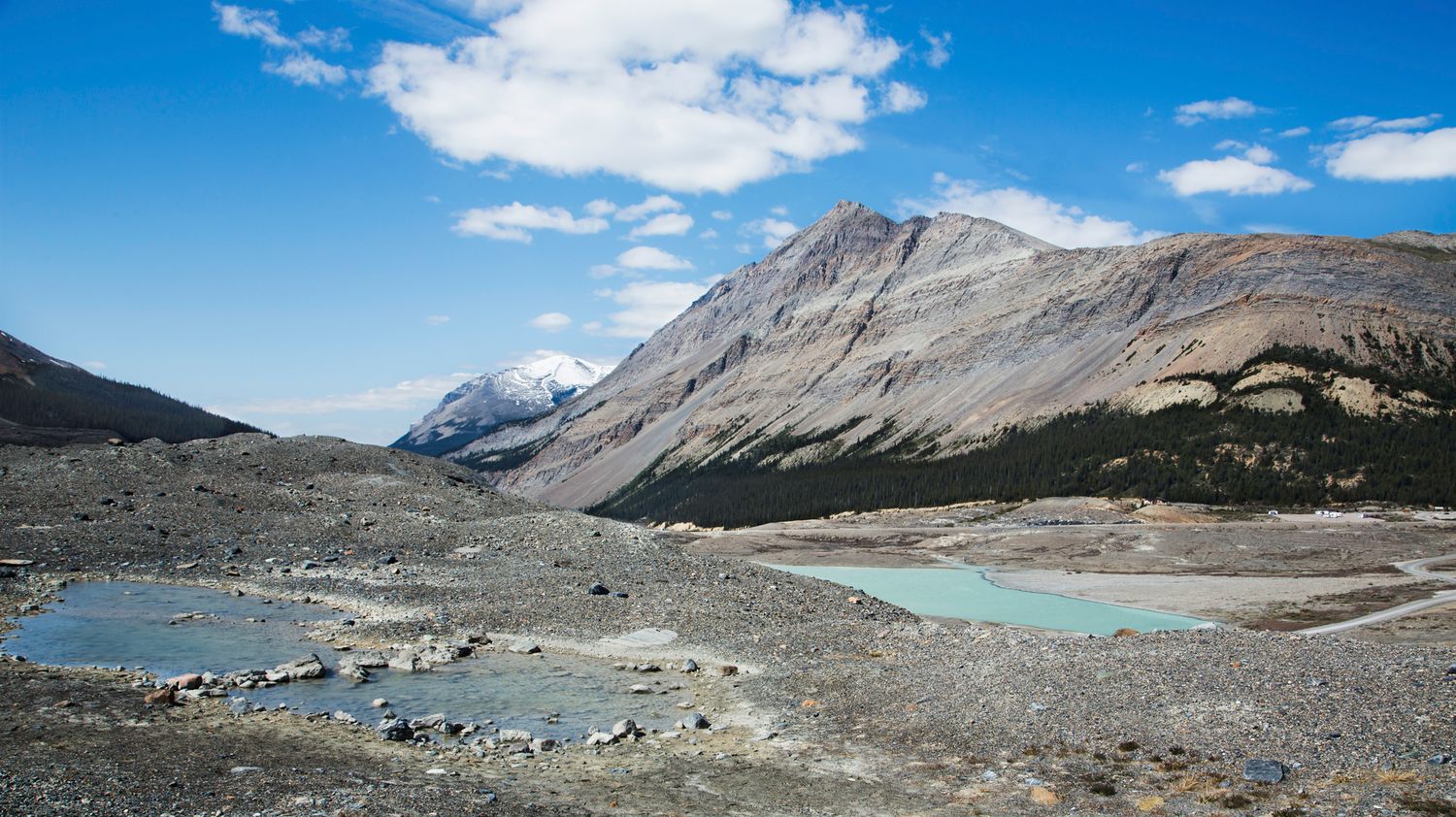 Panoramic mountain vista with turquoise glacial lakes and rocky terrain under blue skies.