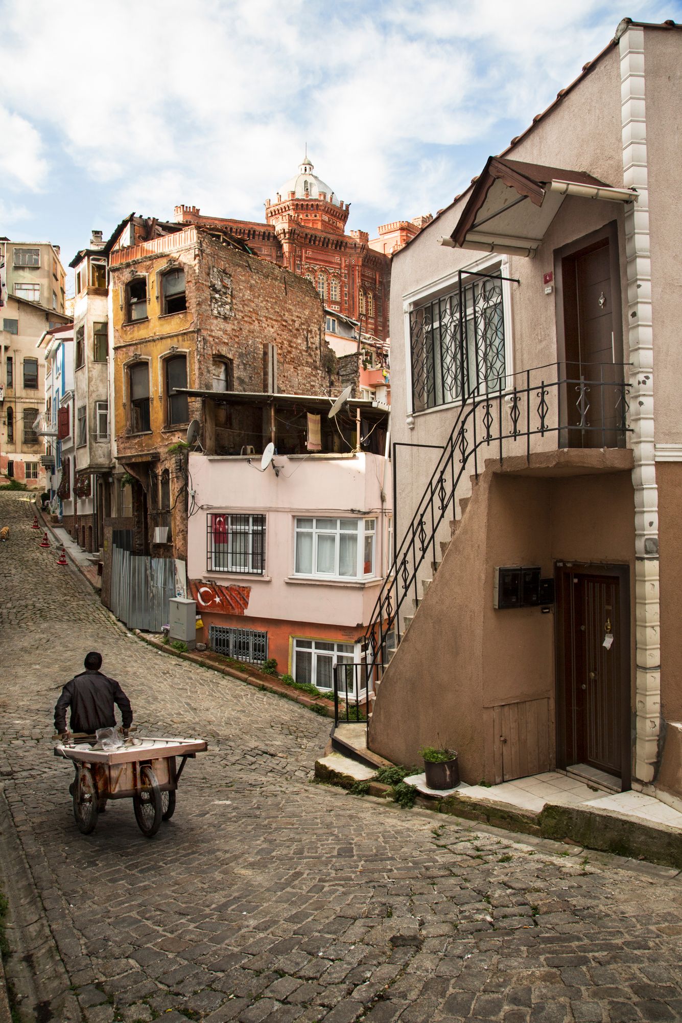 Steep cobblestone street with colorful old buildings and person pushing cart uphill.