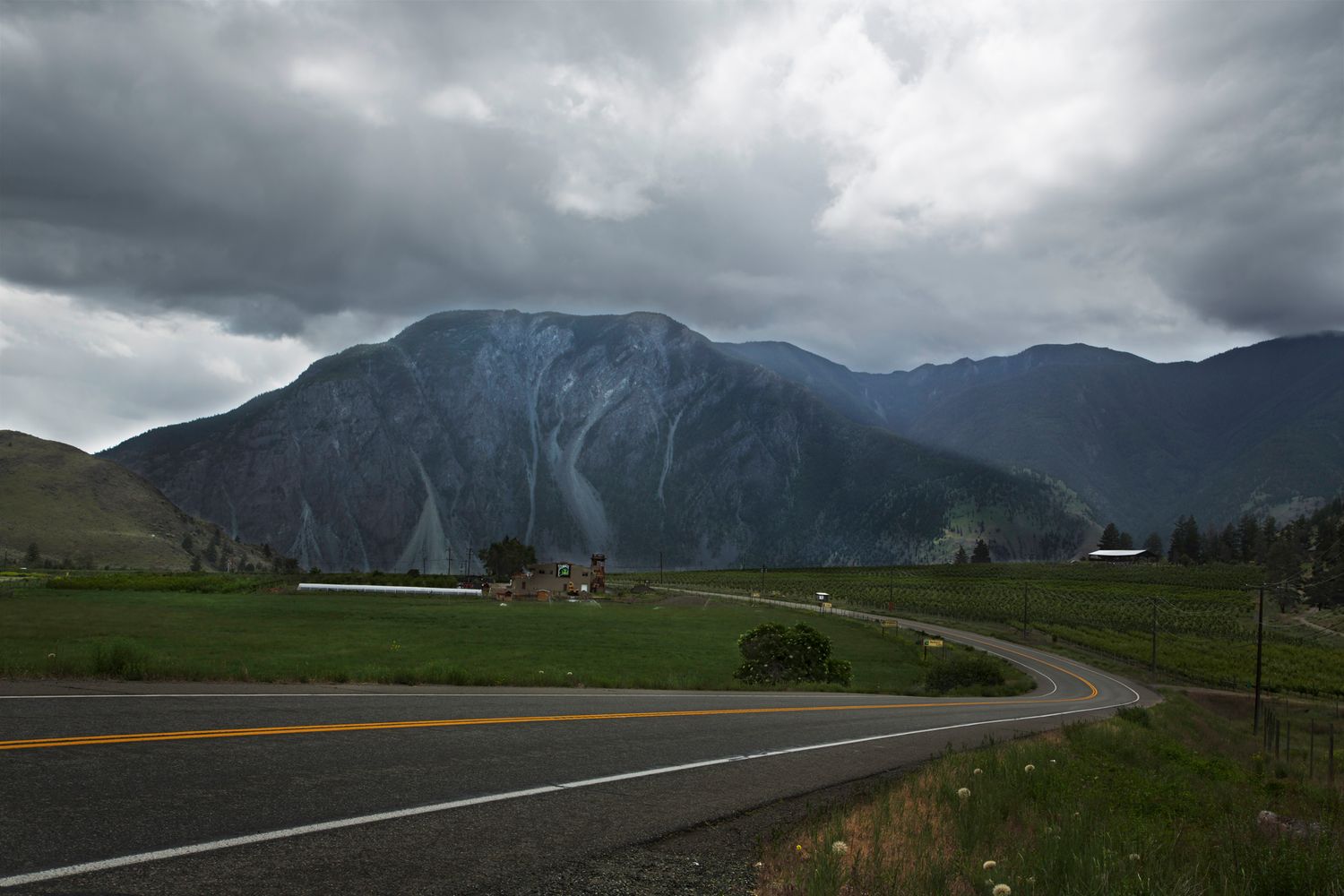 Dramatic mountain landscape with winding road under stormy skies in British Columbia.