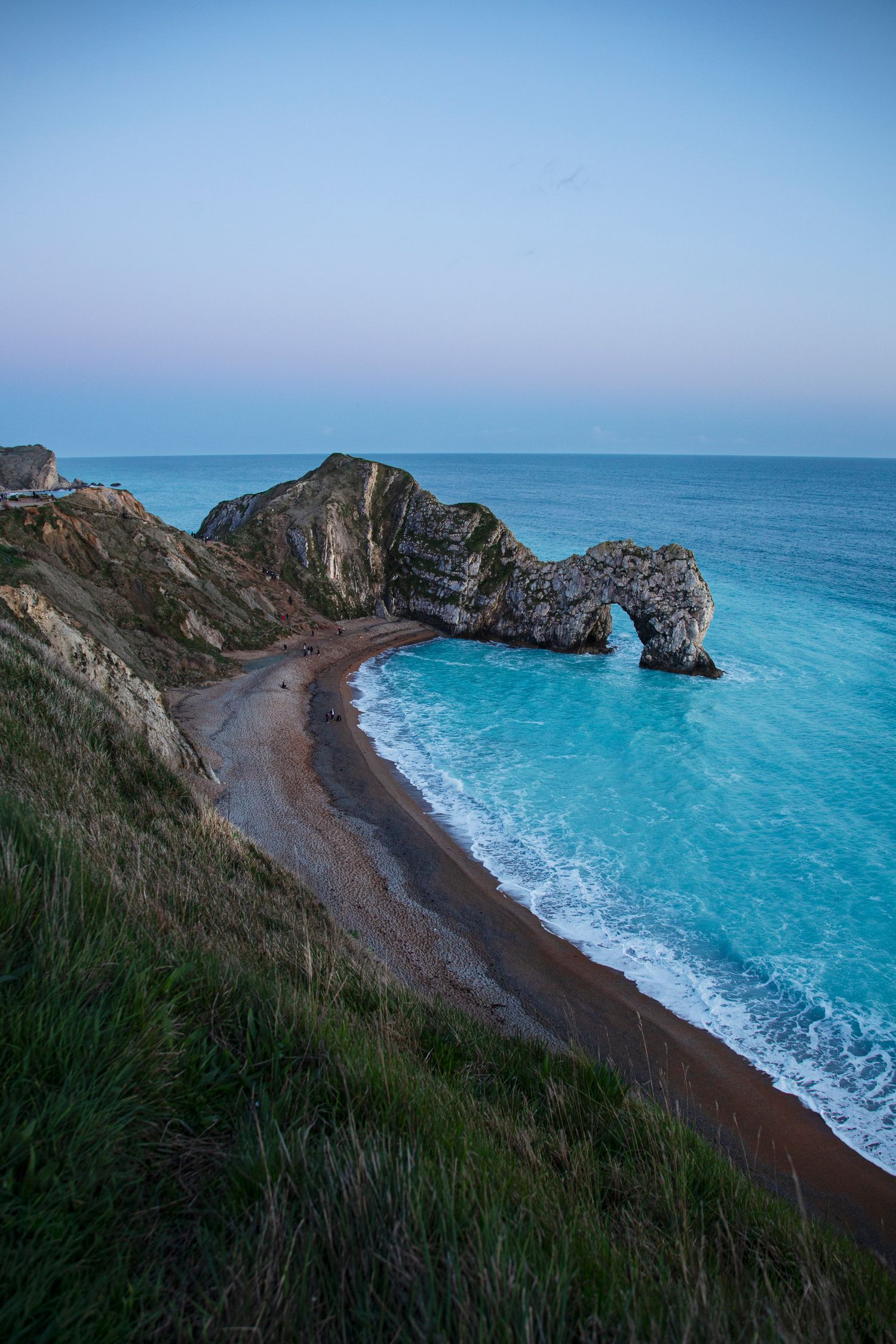 Durdle Door limestone arch frames a pristine turquoise beach cove in Dorset at twilight.